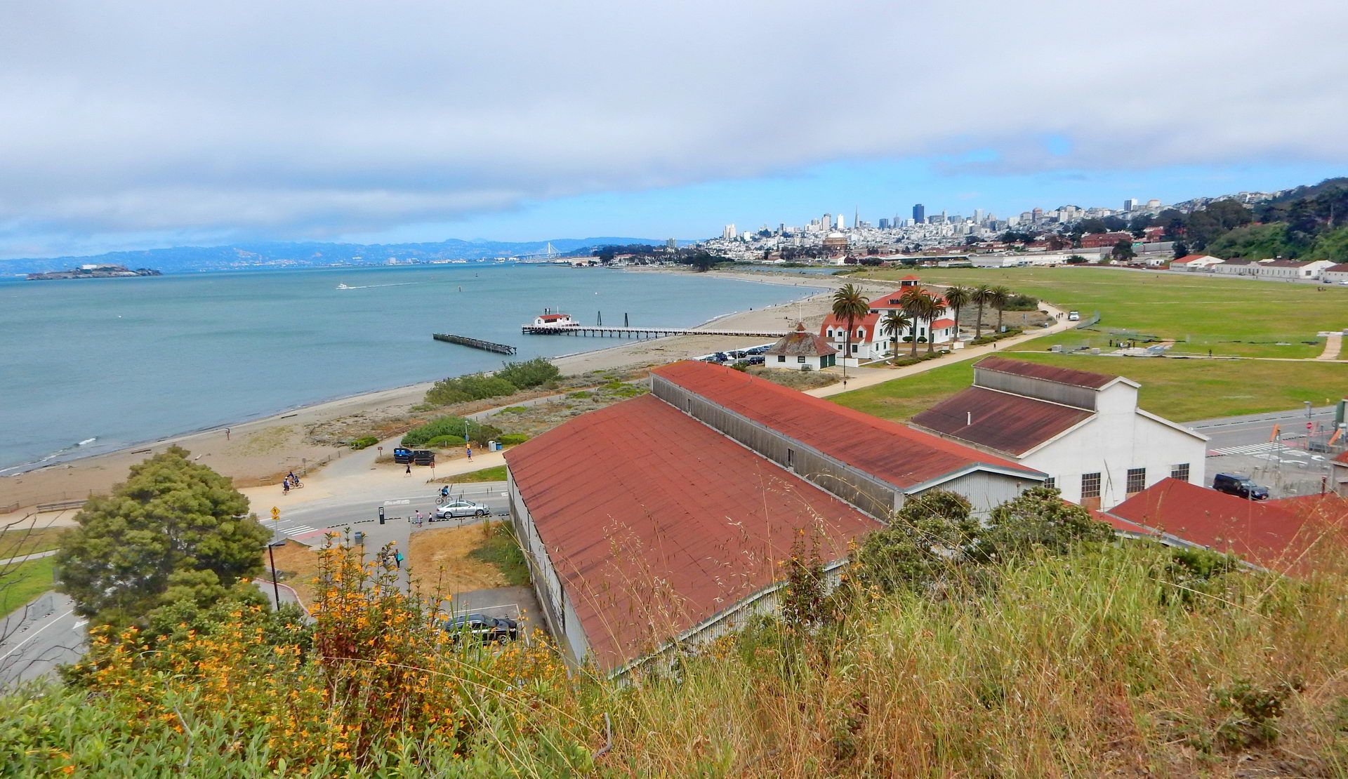 Coastal view with buildings, a beach, pier, and distant city under cloudy sky. - Golden Gate Bridge loop from Larkspur