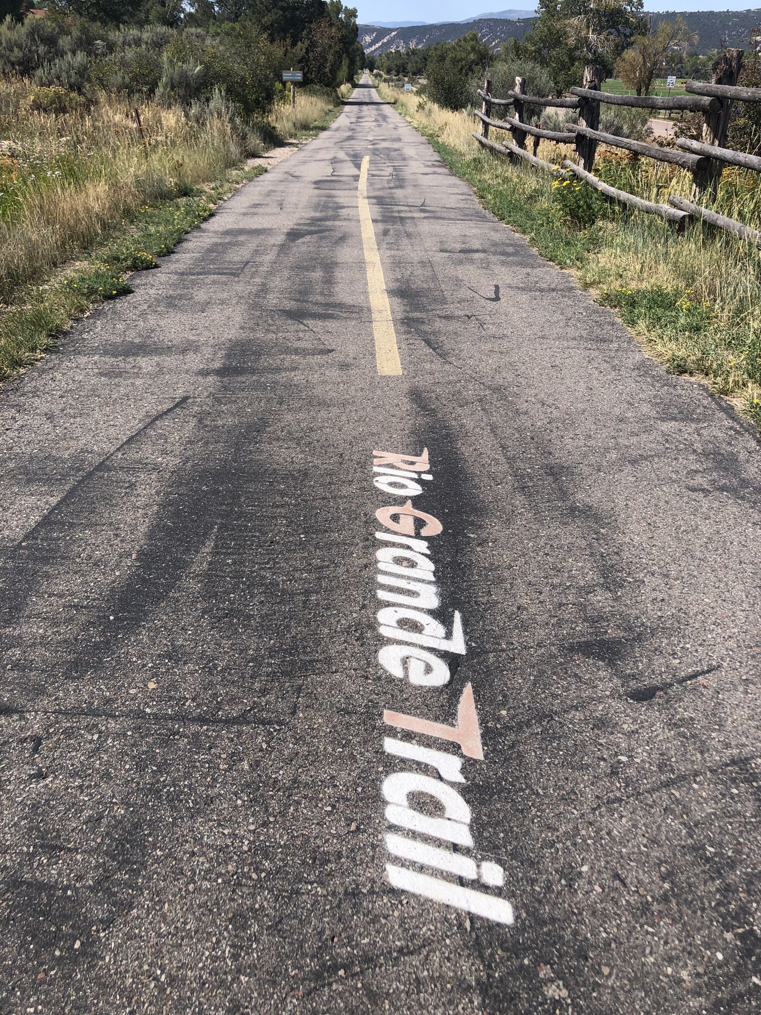 Paved path with painted text, bordered by dry grass and a wooden fence. - Carbondale – Rio Grande Trail loop from Carbondale