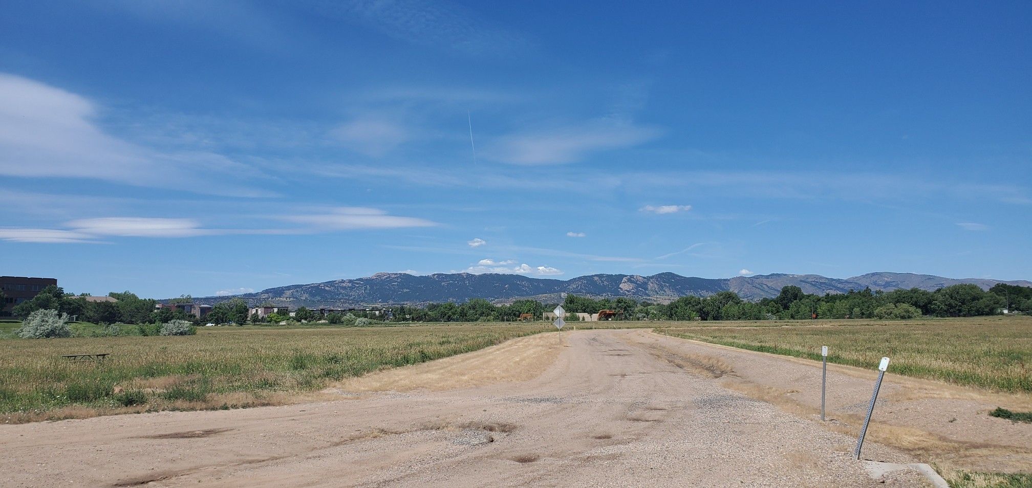 A dirt road leads through grassy fields towards distant mountains under a blue sky. - Mason Trail