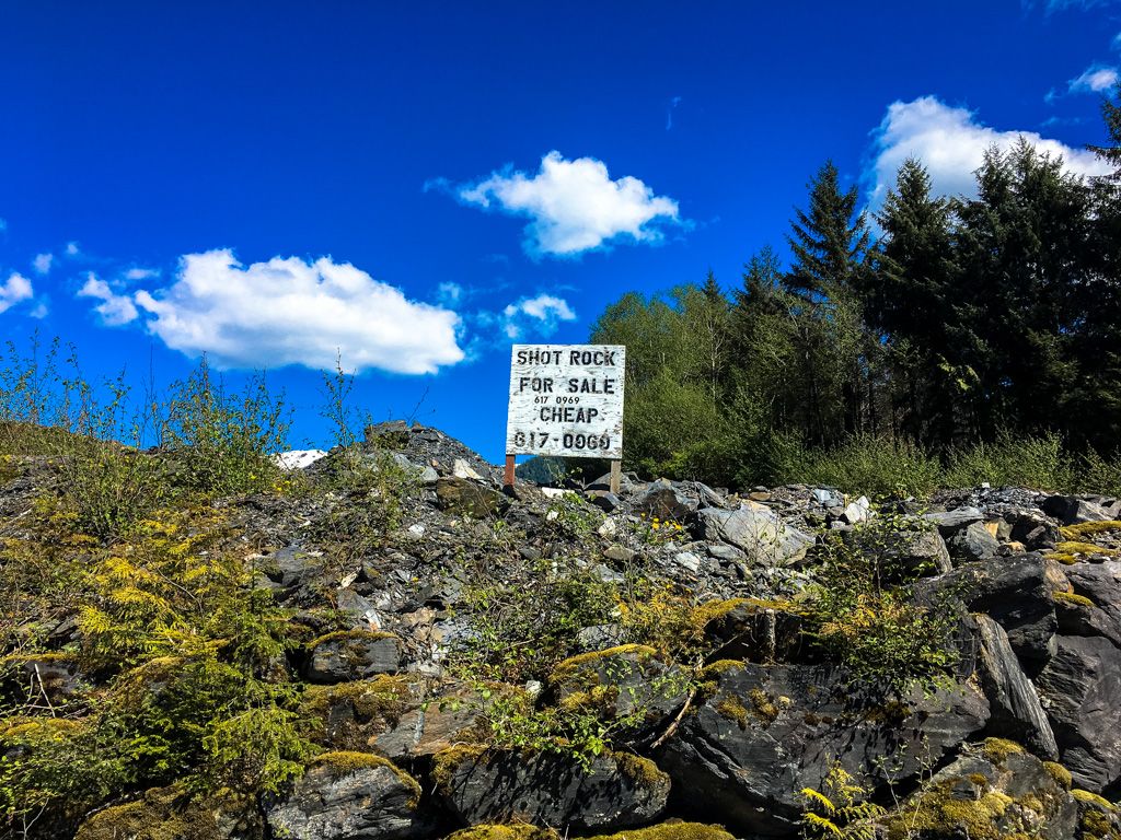 A "Shot Rock For Sale" sign on a rocky, mossy hillside under blue sky. - Pipeline and Ward Creek Loop
