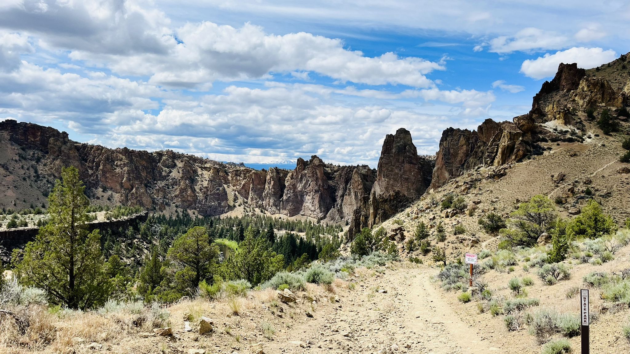 A dirt path winds through an arid canyon with dramatic rock formations under a cloudy sky. - View of Smith Rock State Park – Crooked River loop from Smith Rock State Park
