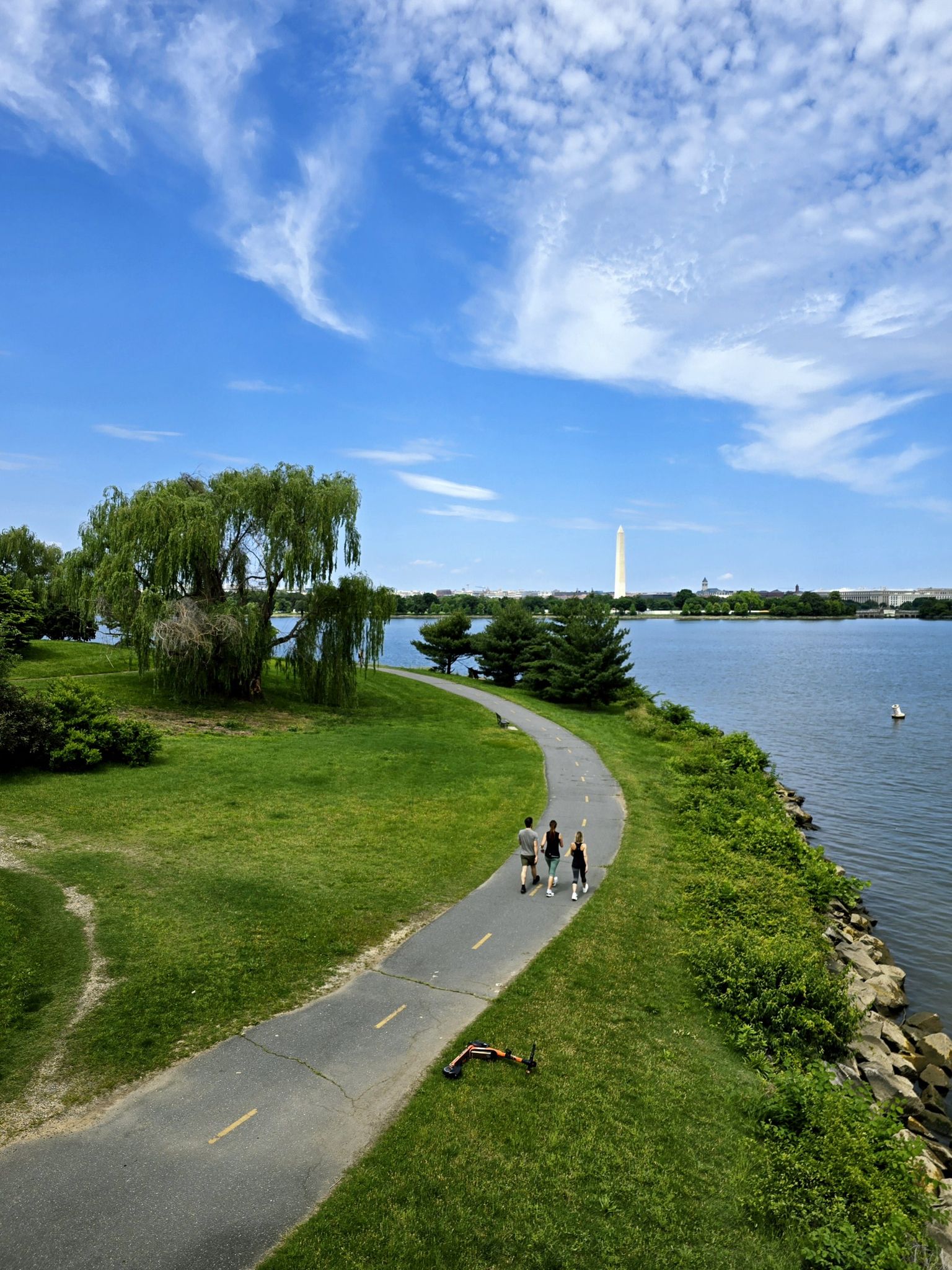 Sunny day with people walking on a path beside the water and distant monument. - Cameron Run – Navy and Marine Memorial loop from Van Dorn Street