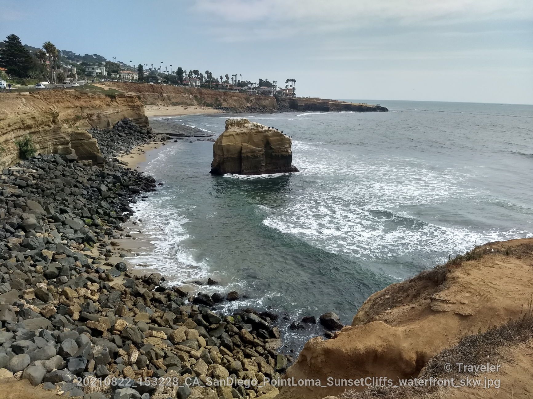 Rocky beach with a large sea stack in the water under a cloudy sky. - Sunset Cliffs Coastal Trail