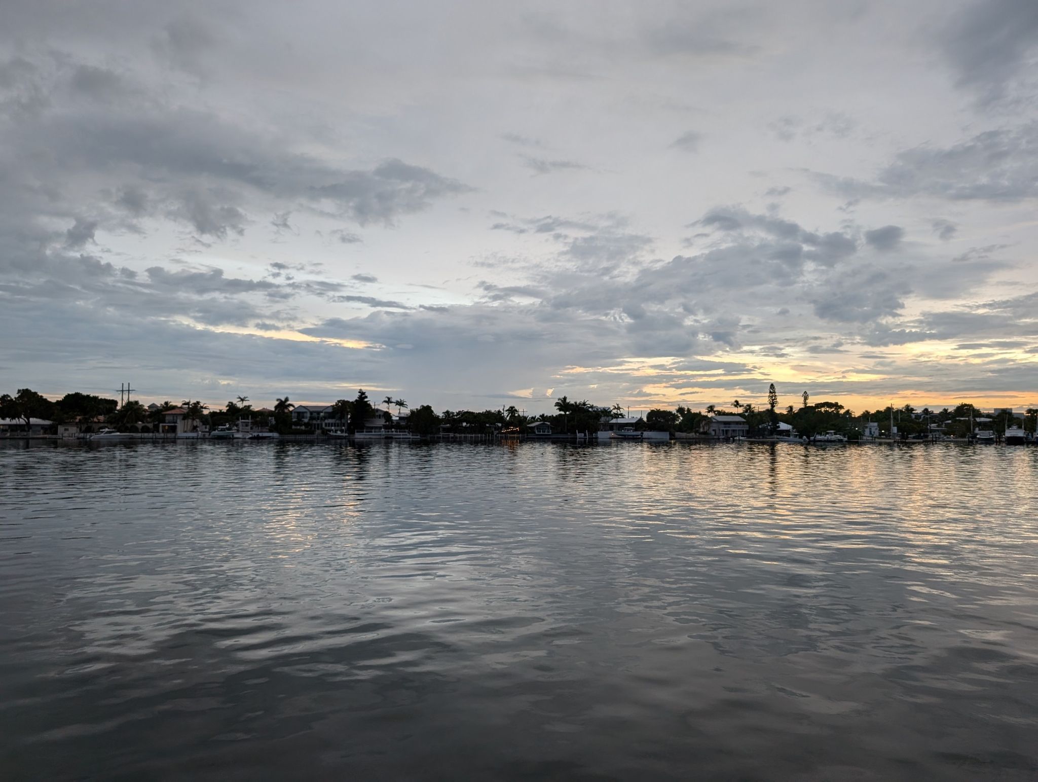 Calm water reflecting a distant town skyline under a cloudy sunset sky. - Historic House in Key West – St. Pauls Episcopal Church loop from Key West