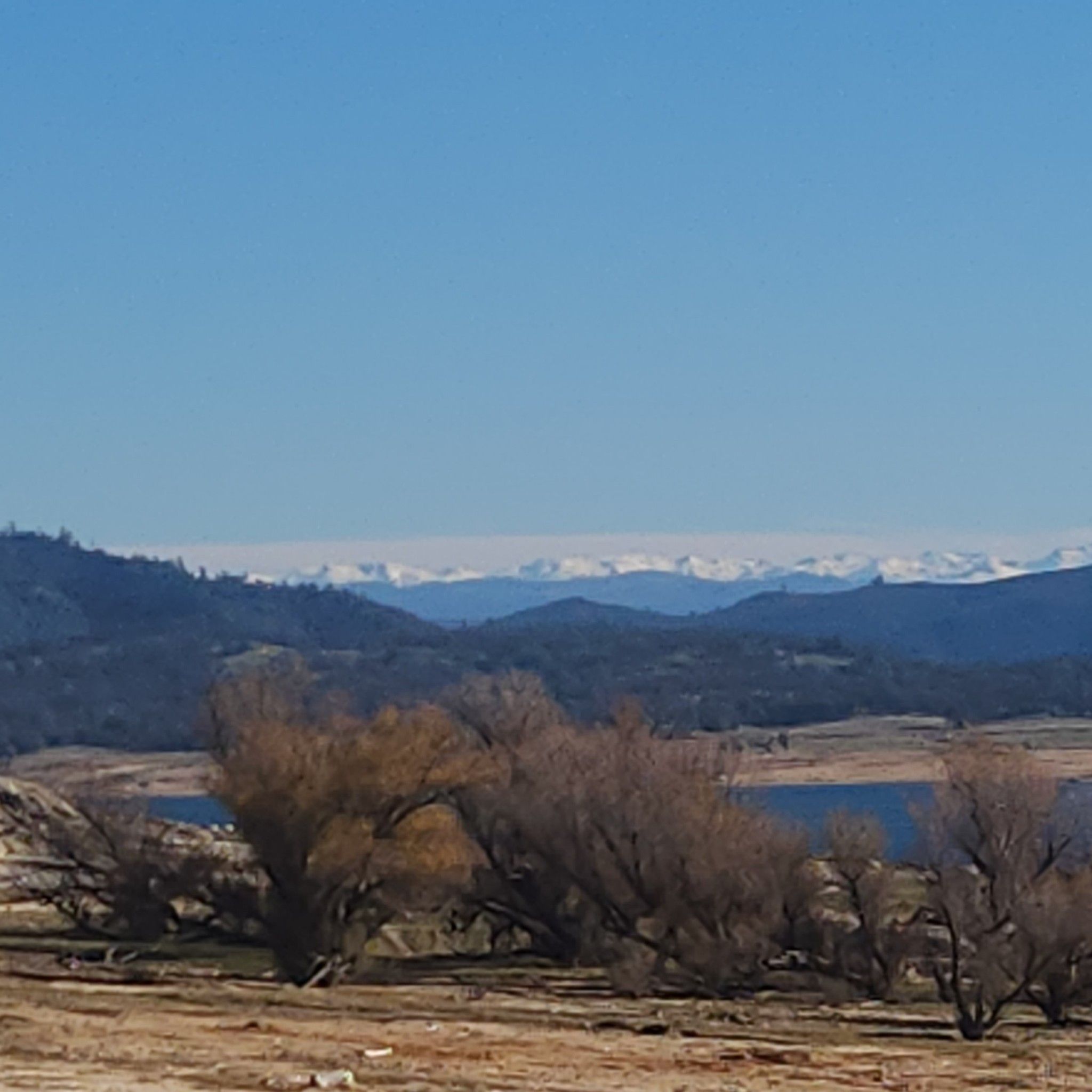 Distant snow-capped mountains over a lake and dry, hilly landscape. - Granite Bay to Beals
