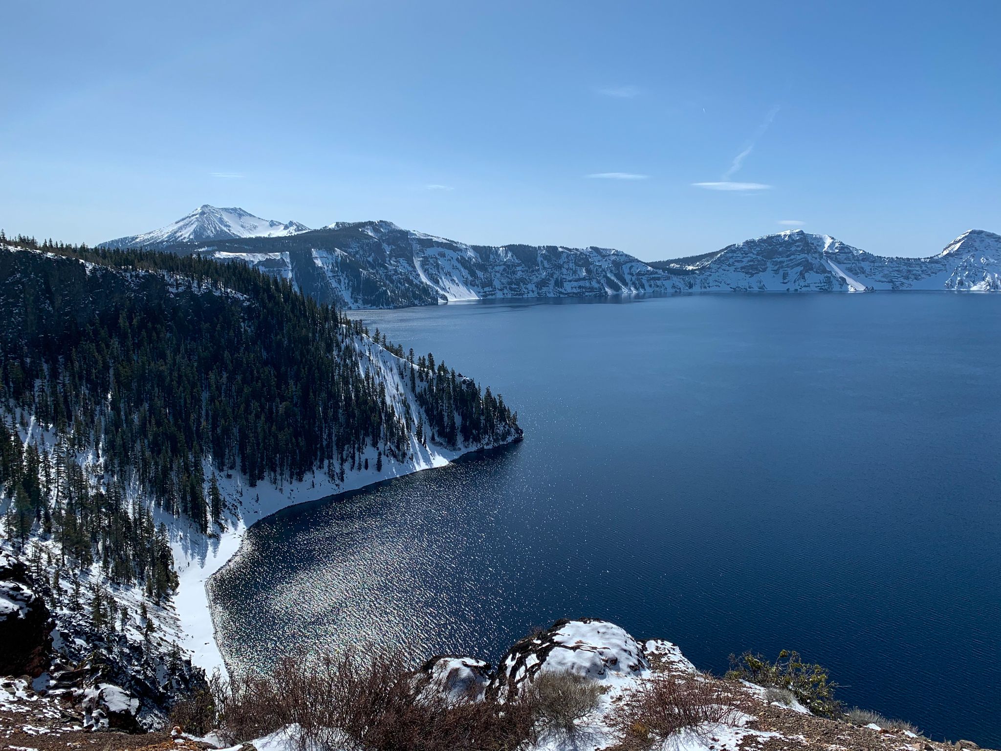 Vast blue lake surrounded by snow-covered mountains and evergreen forests on a clear day. - Cleetwood Cove to Skell Head