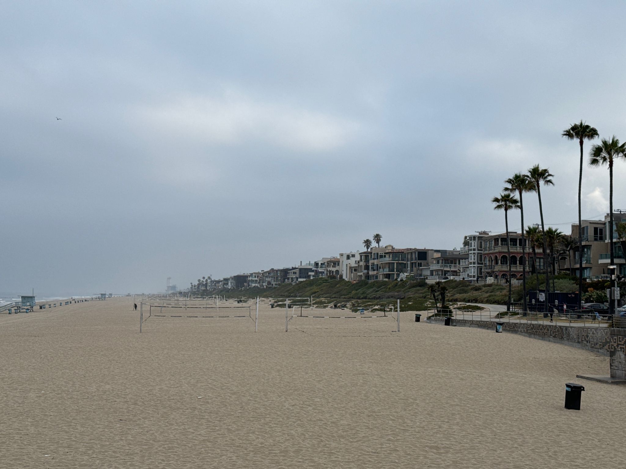 Overcast beach with volleyball nets, distant houses, and palm trees. - Manhattan Beach to Redondo Beach via the South Bay Bike Path