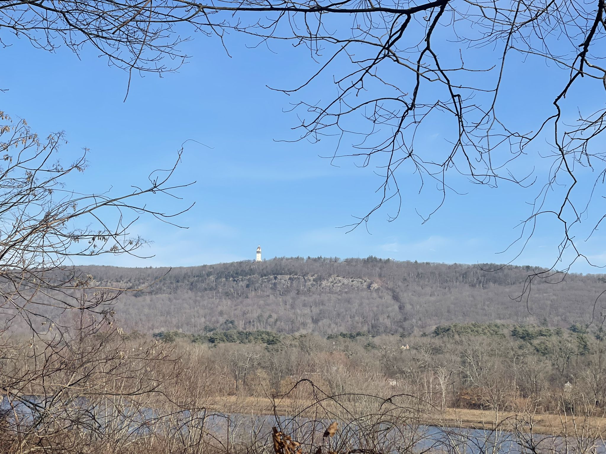 Distant white tower on a forested hill under a clear blue sky. - East Coast Greenway loop from Weatogue