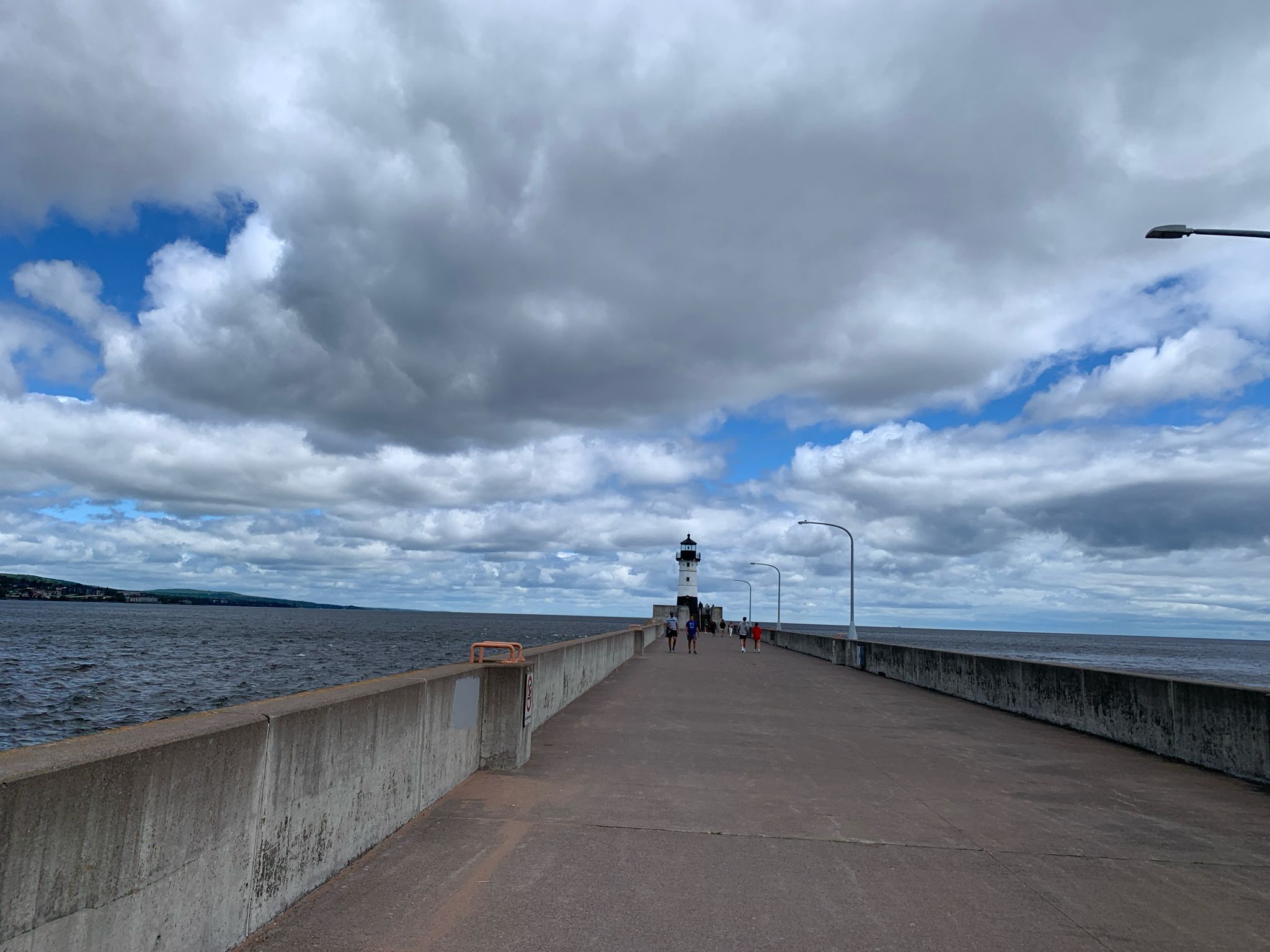 People walk on a long pier towards a lighthouse under a cloudy sky. - Superior Hiking Trail: Canal Park to Enger Park