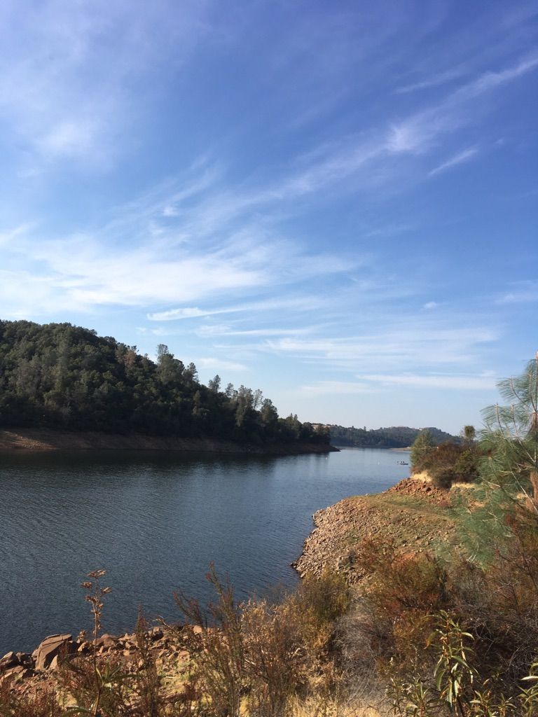 A wide lake with forested hills and a rocky shore under a bright sky. - Darrington and Sweetwater Trail