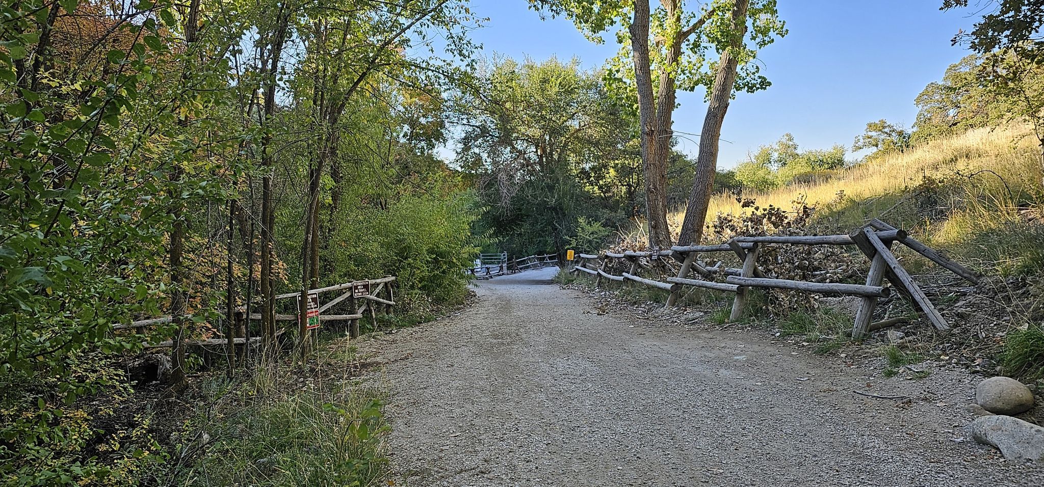 Gravel path winding through green trees with a wooden fence, bright daylight. - Ghost Falls via Lower Corner Canyon Trail