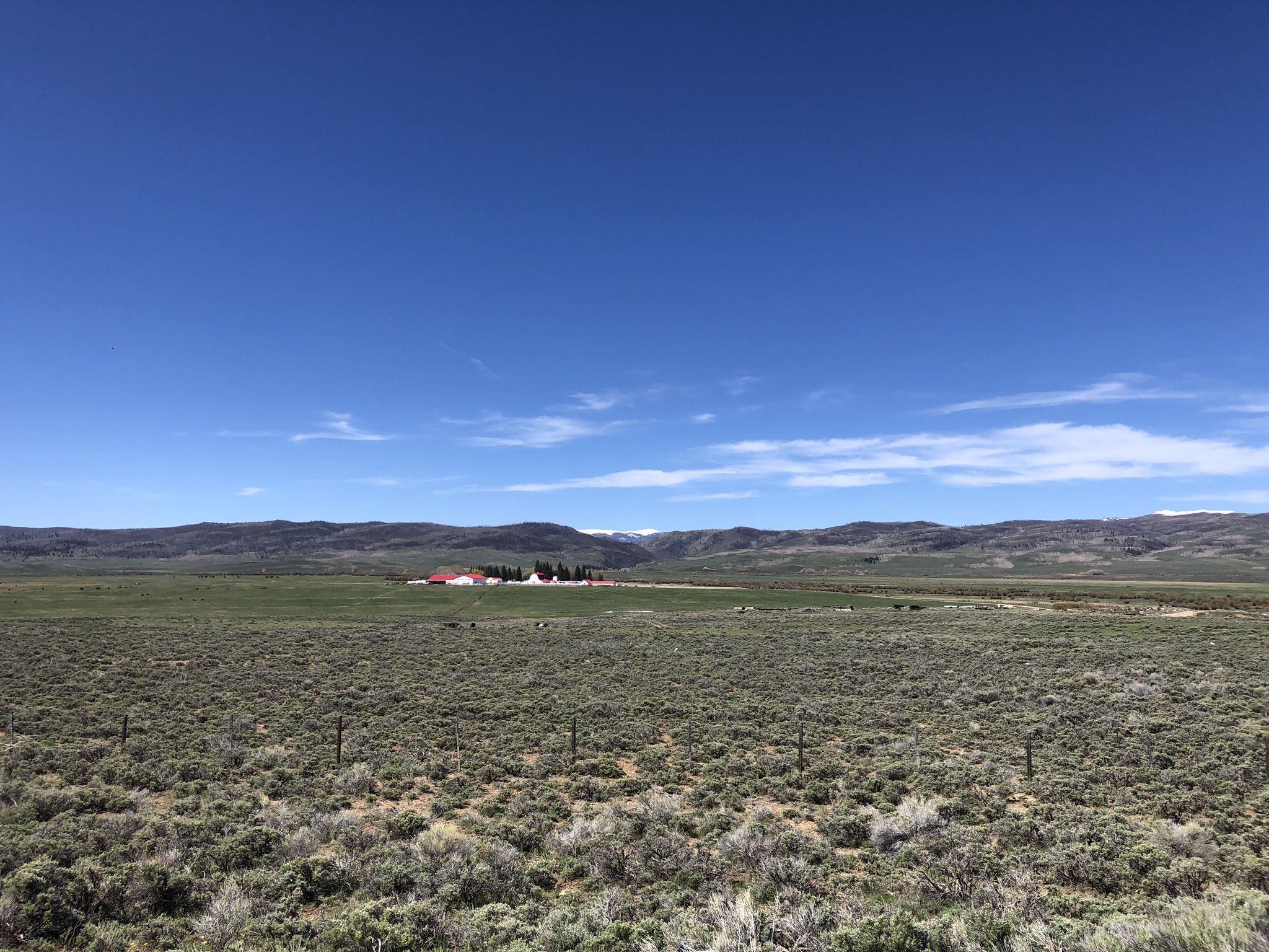 Vast arid landscape with distant red-roofed buildings under a clear blue sky. - TransAmerica Trail: Encampment to Colorado State Line