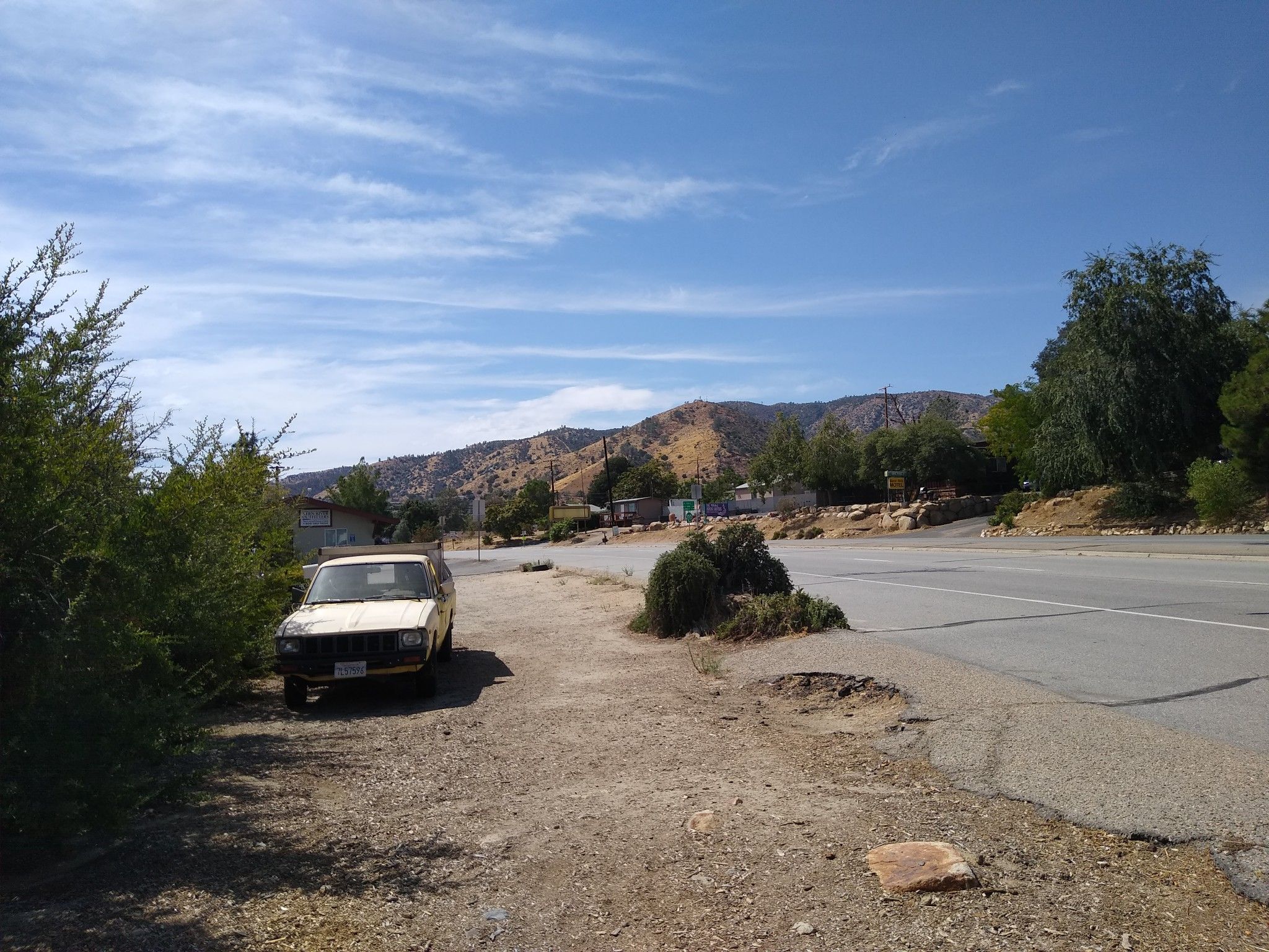 An old car parked on a dirt shoulder next to a road, with hills. - Lake Isabella and Silver City Ghost Town loop