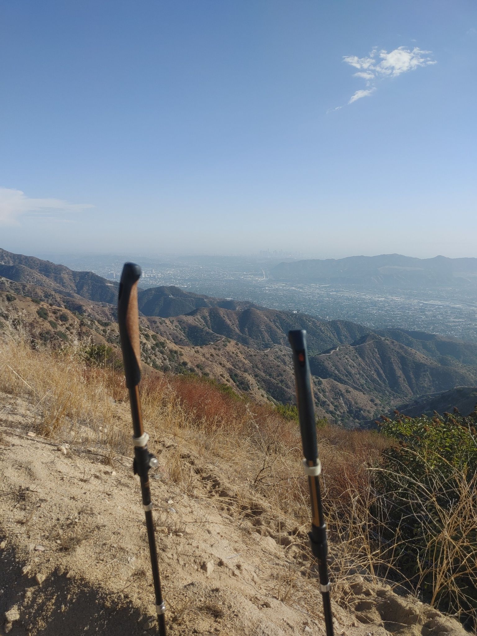 Two hiking poles stand on a dry mountain path, overlooking a hazy valley. - LA City Open Space – MRCA Open Space loop from Haines Canyon Park