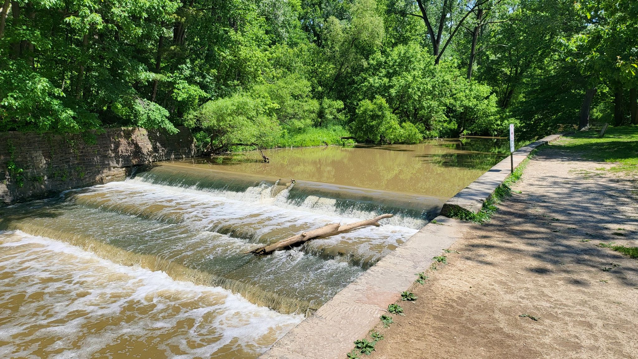 Sunny view of a small waterfall with green trees and concrete banks. - Rocky River Nature Center – Quiet all purpose trail loop from Berea