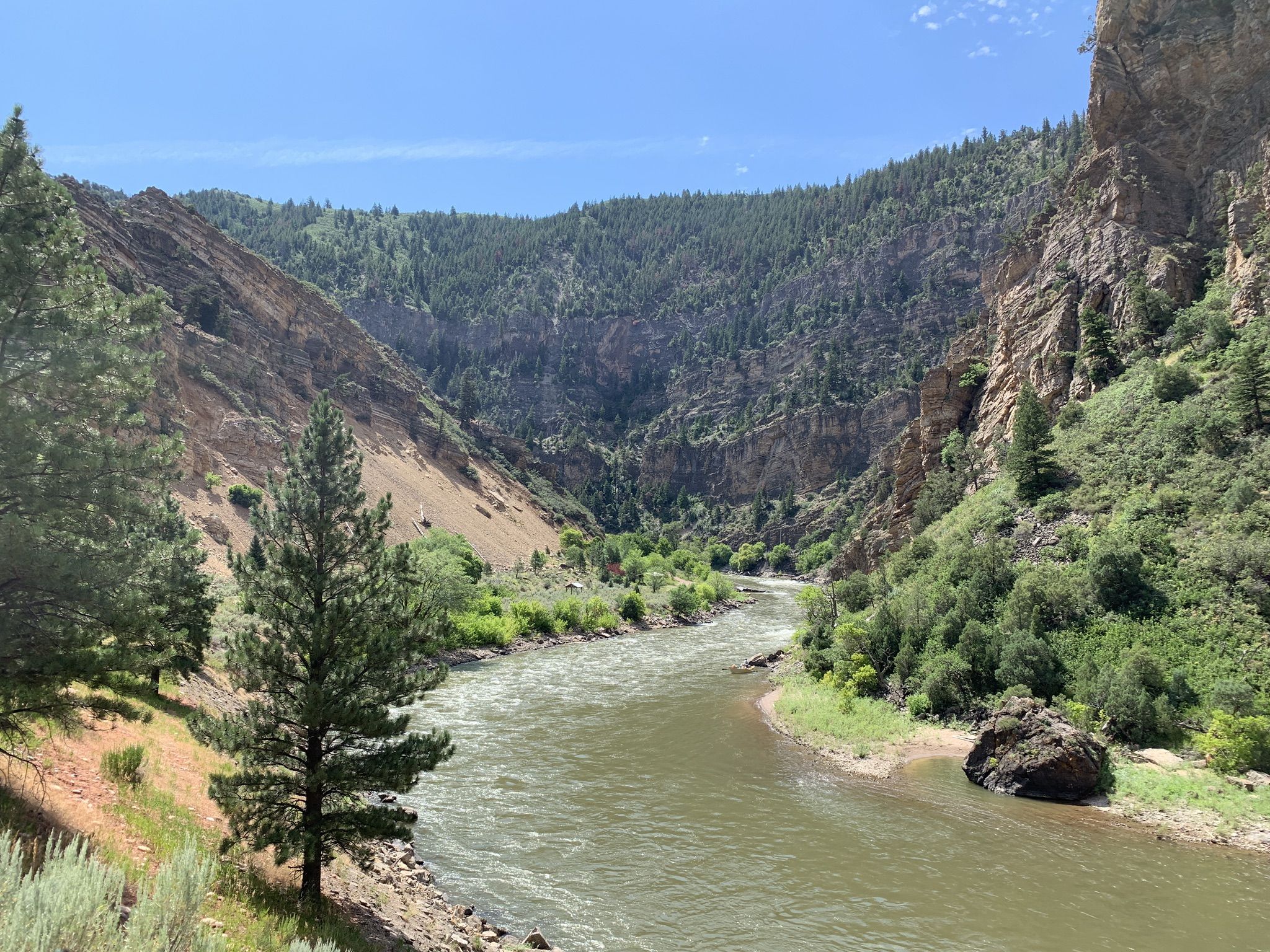River winding through a forested canyon with steep, rocky slopes under a bright blue sky. - Glenwood Canyon Trail