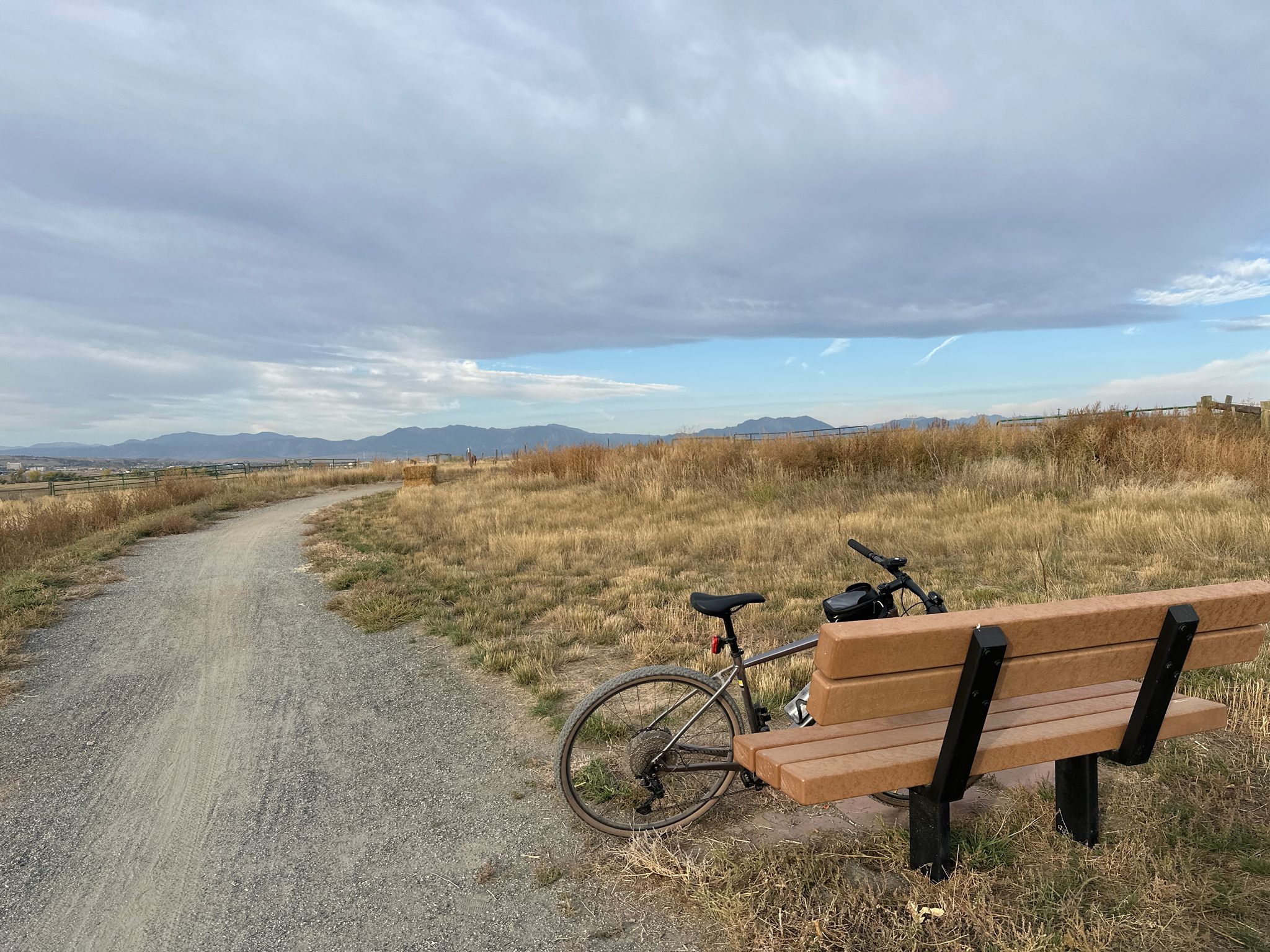 A bicycle parked next to a wooden bench on a gravel path, cloudy sky. - Cradleboard Trail – Sterns Lake loop from Admor Open Space