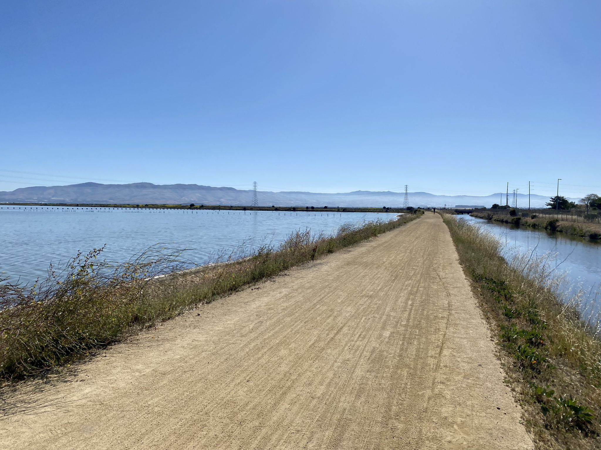 Sunny dirt path between water and distant mountains under a clear blue sky. - Moffett Federal Airfield loop from Lockheed Martin
