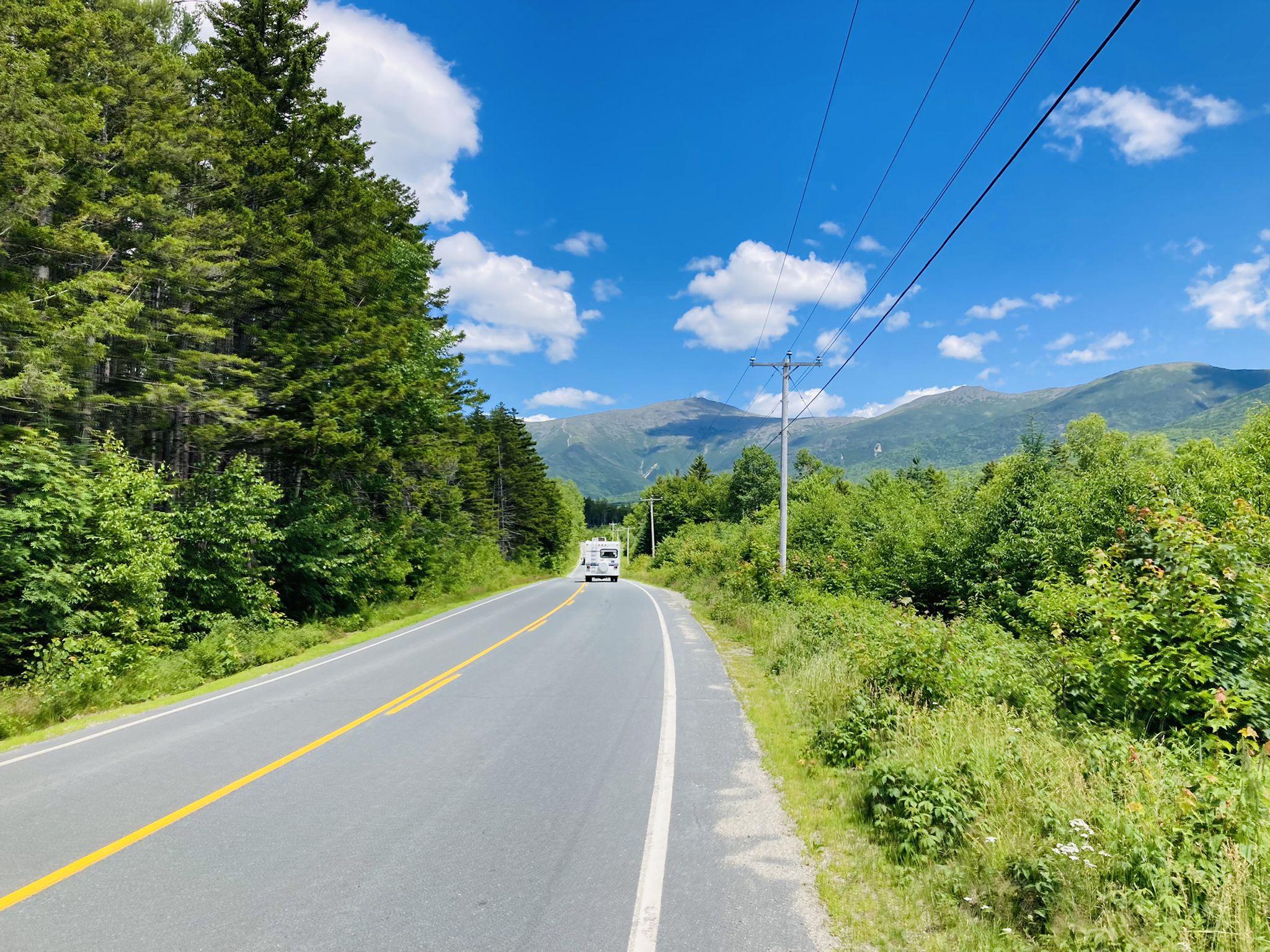 Paved road with a white vehicle, surrounded by forest and distant mountains. - Base Station Road & Mount Clinton Road loop