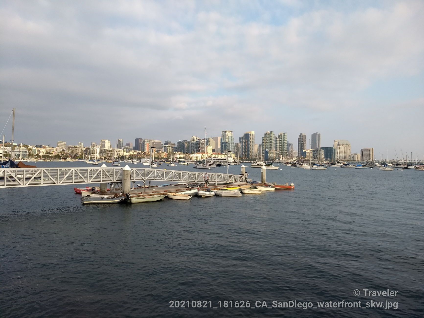 A long pedestrian bridge over water with boats and a city skyline. - Spanish Landing Monument – Spanish Landing Park loop from Point Loma