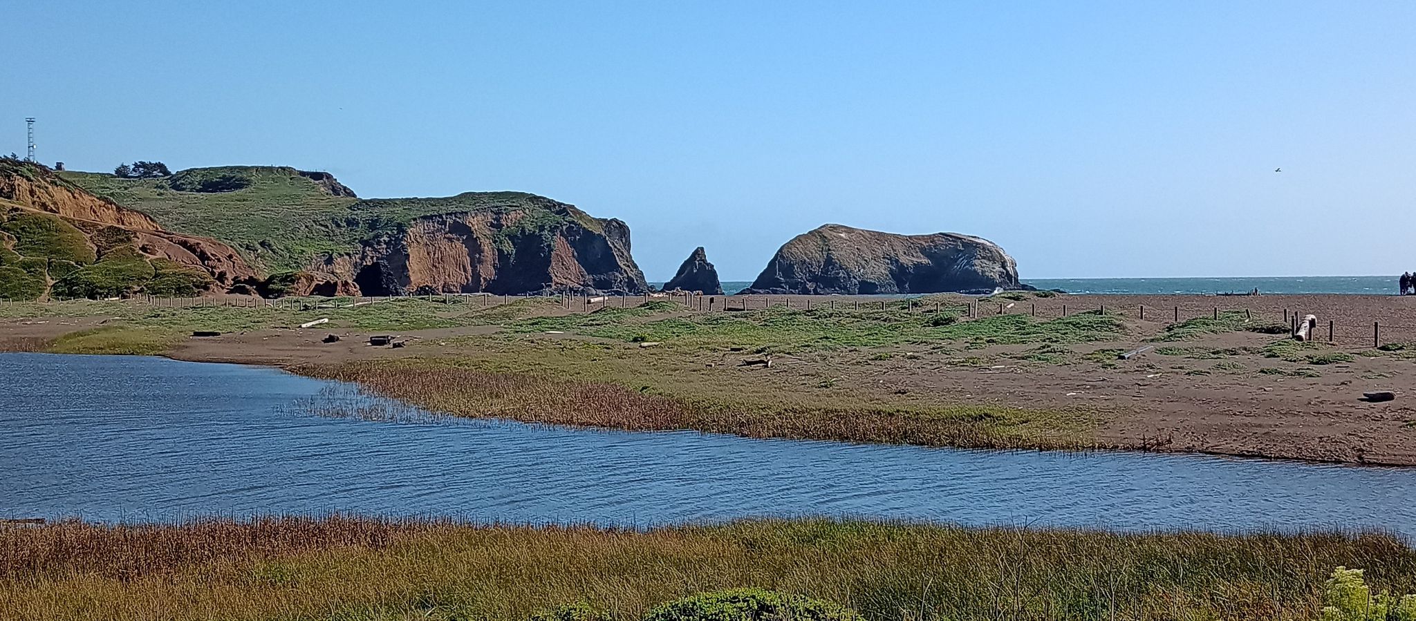 Sunny coastal landscape with calm water, marsh, sandy beach, and rocky cliffs. - Coastal, Wolf Ridge, and Miwok Trails Loop