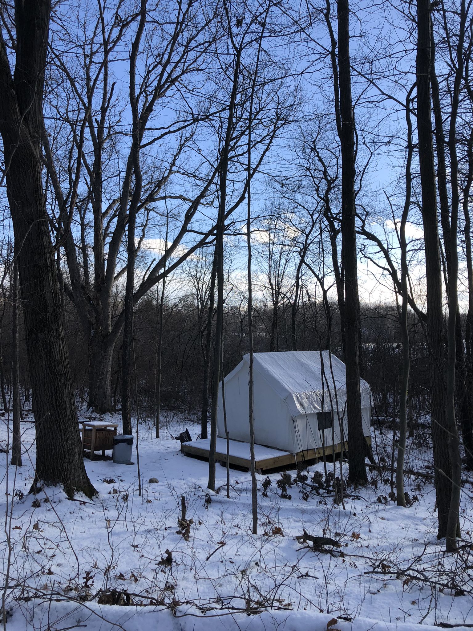 A white canvas tent stands on a snowy forest floor among bare trees. - Haven Hills Natural Area loop