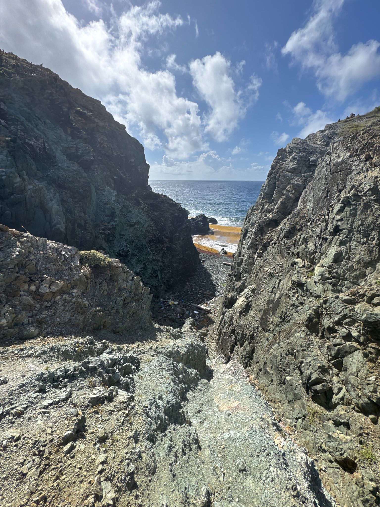 Rocky gorge opens to a small sunlit beach and blue ocean. - Ram Head Trail