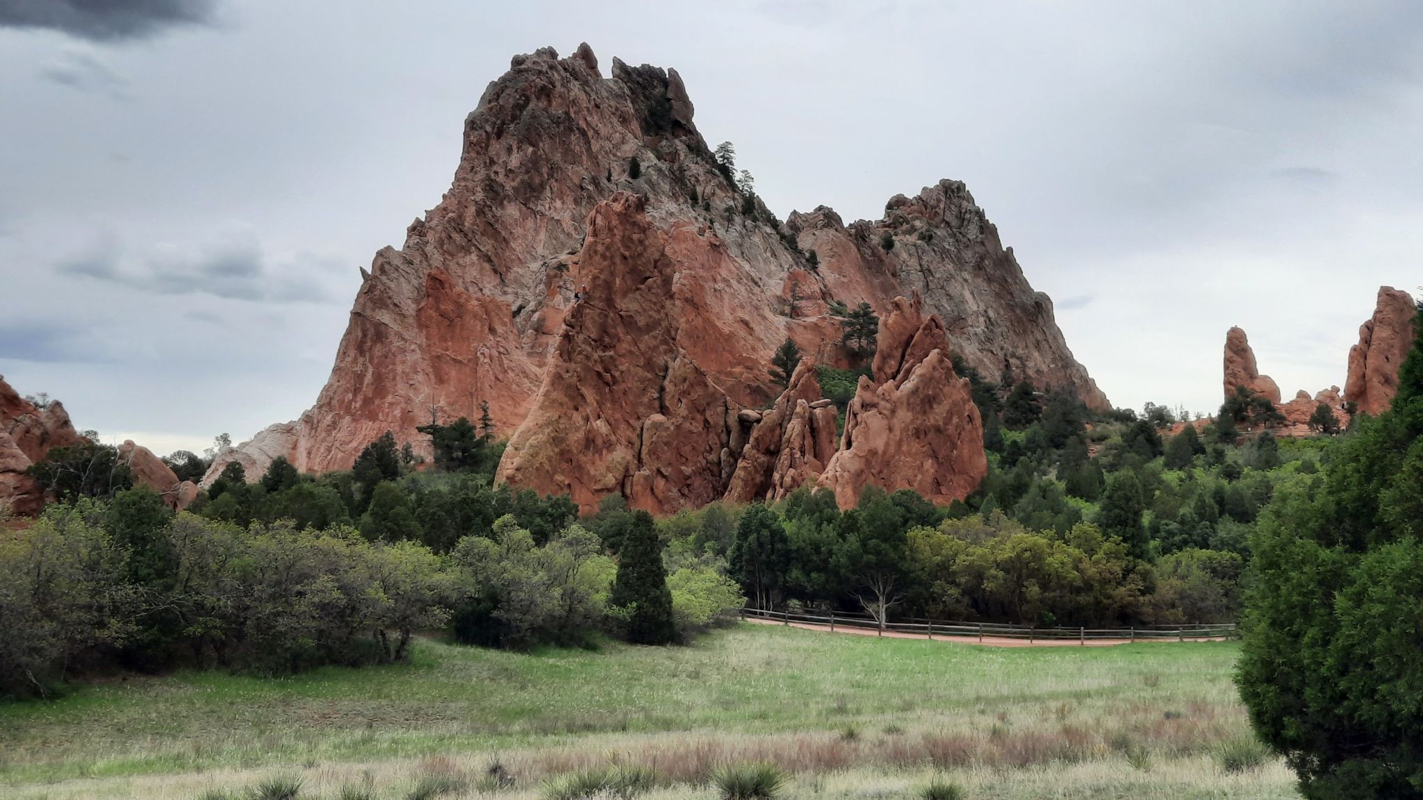 Large red rock formations rise above a green field under a cloudy sky. - Gateway Trail to Palmer Trail and Scotsman Trail Loop