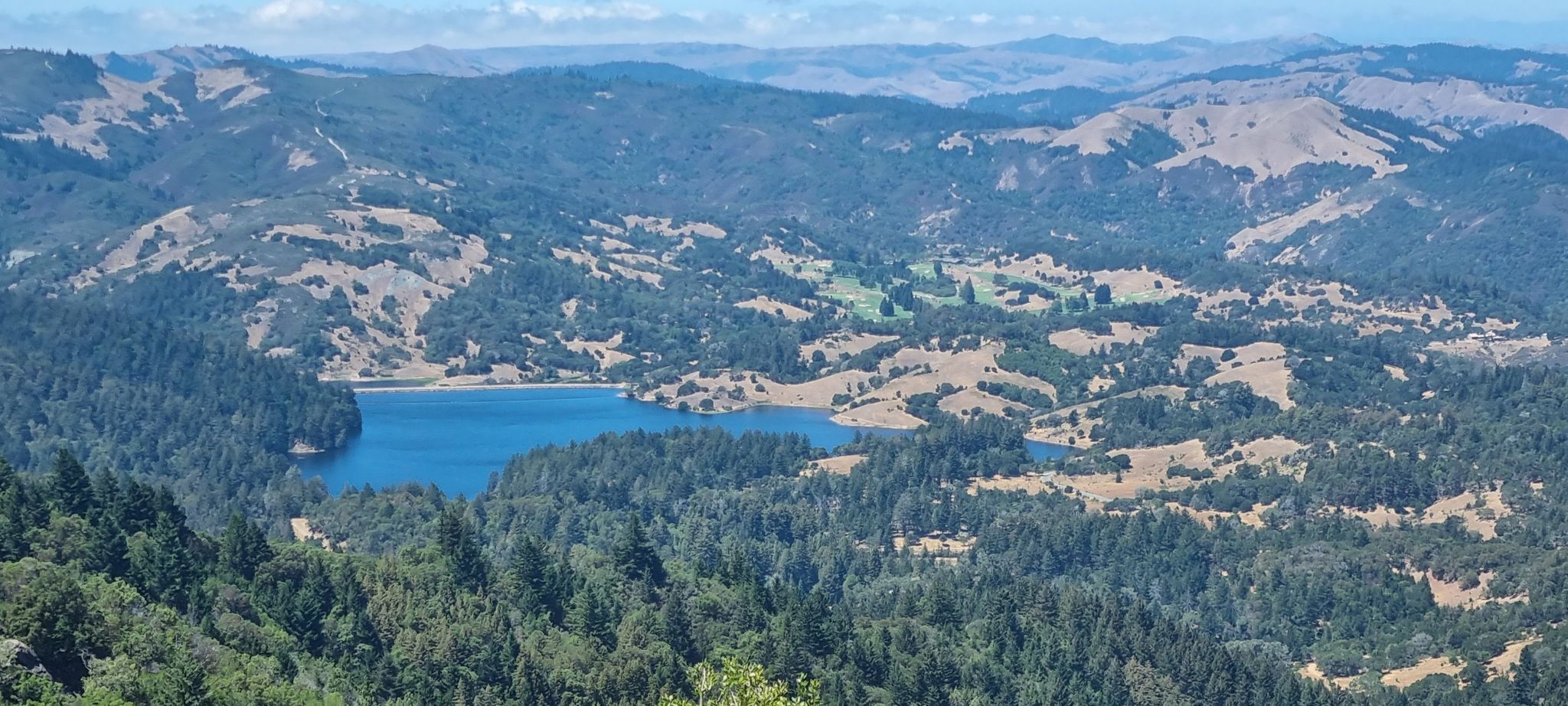 Panoramic view of a bright blue lake nestled among green and golden hills. - Eldridge Grade Fire Road