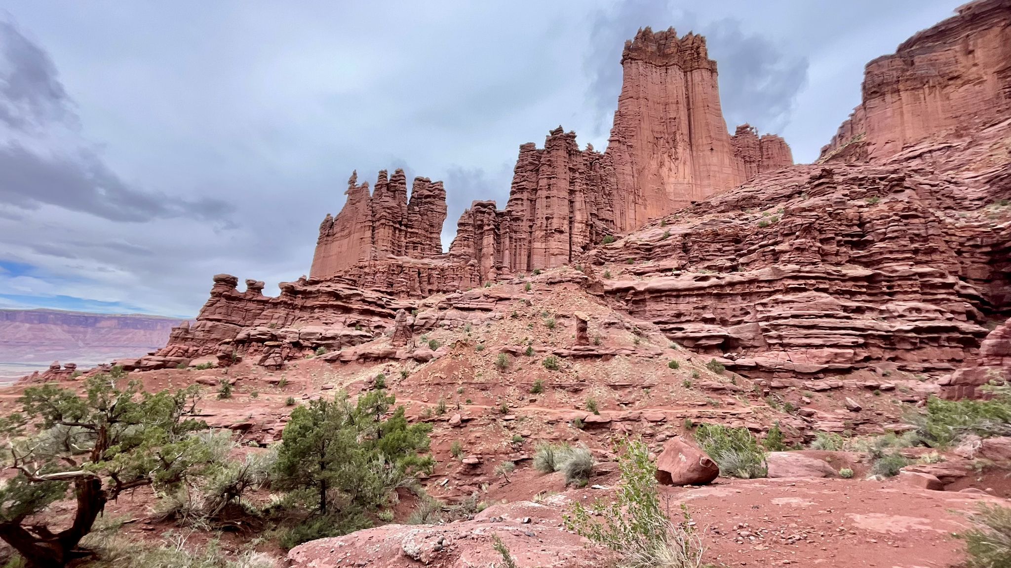 Rugged red rock formations and cliffs with sparse vegetation under a cloudy sky. - Fisher Towers Trail