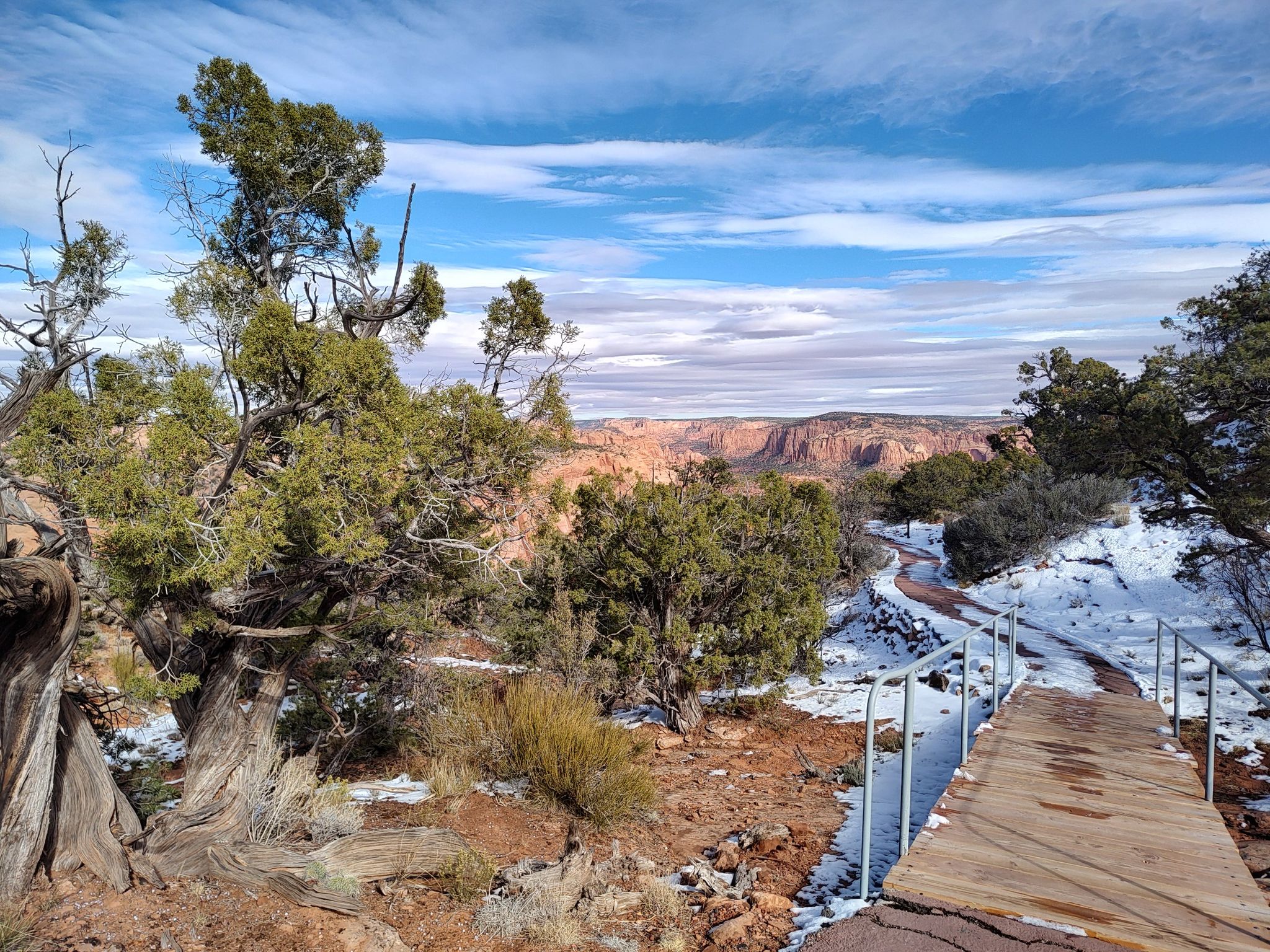 Wooden boardwalk with snow, leading to a vast desert canyon view. - Sandal Trail