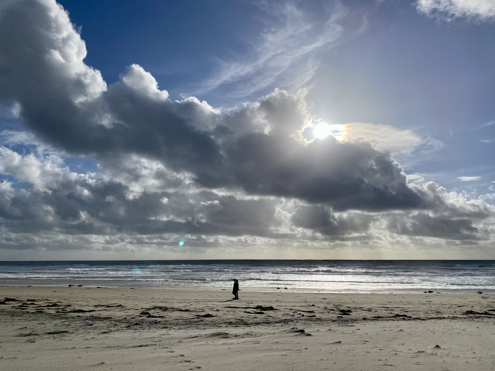 Lone person walking on a wide, sunny beach under dramatic clouds. - SDSU Beach – Mission Bay loop from Pacific Beach