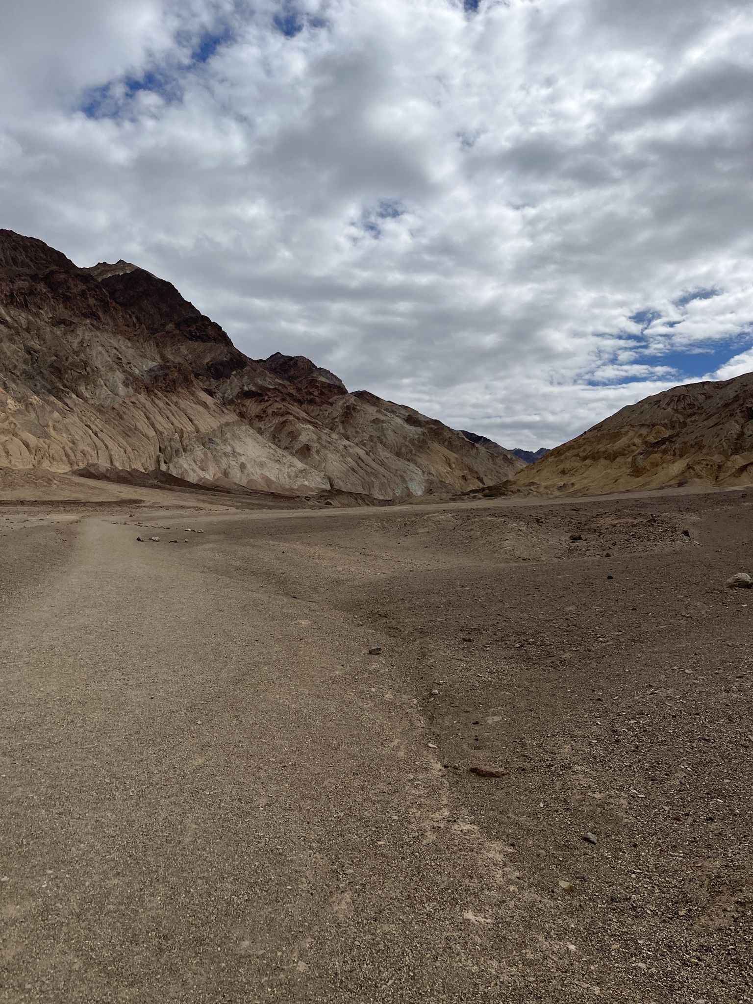 Wide desert wash leads to colorful mountains under a cloudy sky. - Desolation Canyon Trail