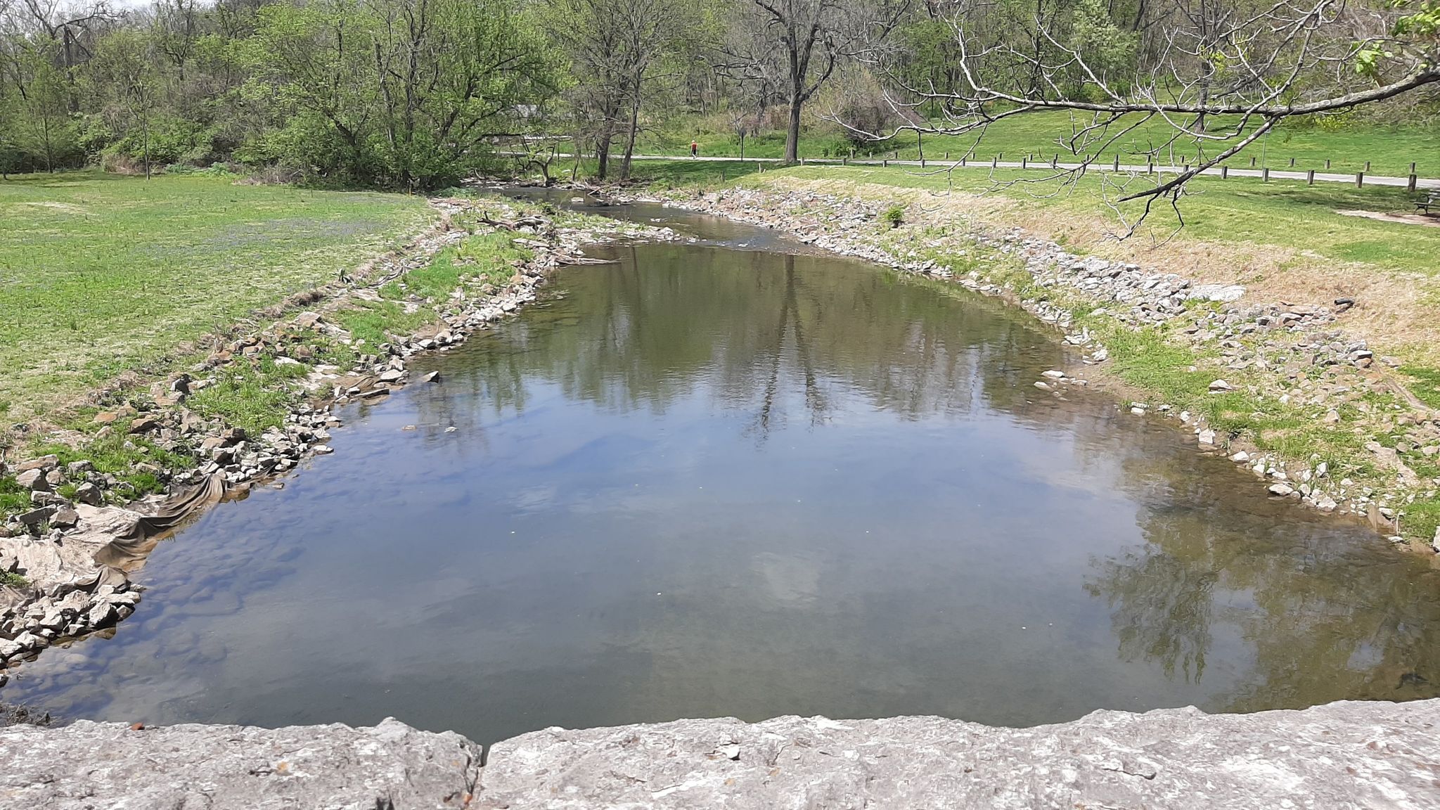 A calm river flows between green grassy banks under bright daylight. - Seneca Park and Bowman Field Loop