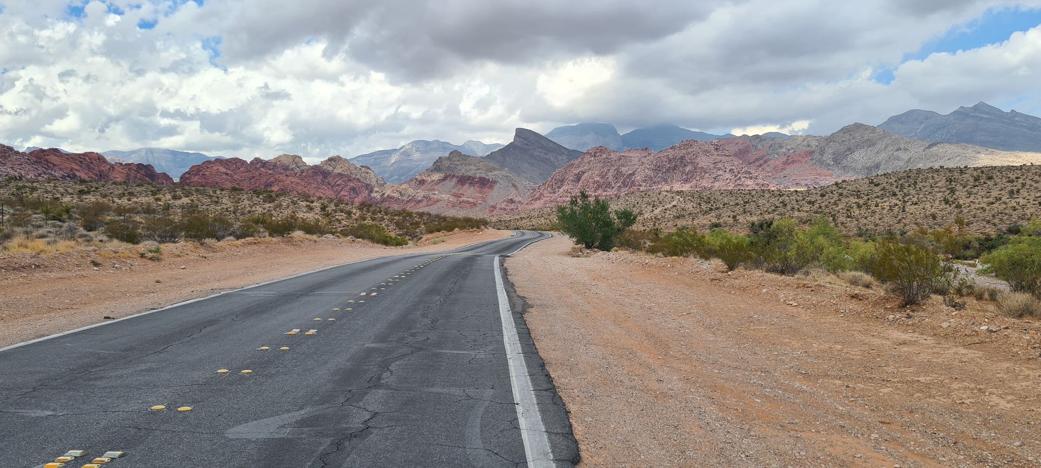 Winding desert road with red rock formations under an overcast sky. - Cannibal Crag loop from Summerlin