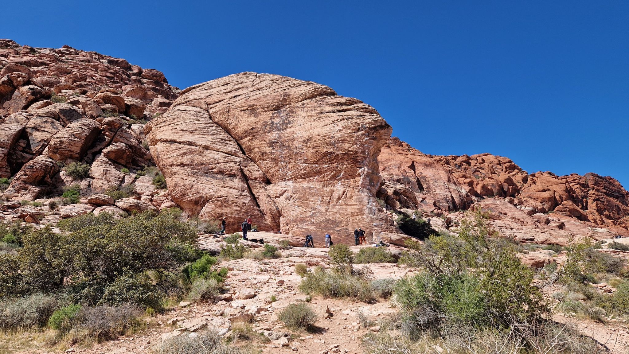 Group of people gathered near a massive red rock formation under a clear sky. - Cannibal Crag loop from Summerlin