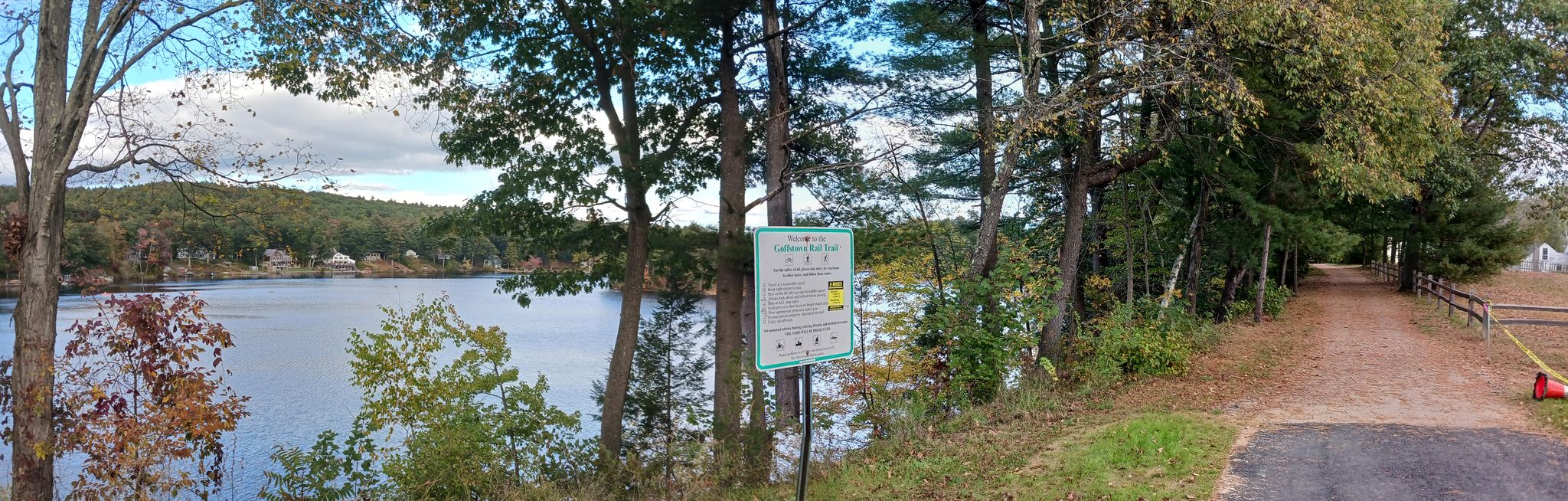 Panoramic view of a lake, dense forest, and a dirt path on an overcast day. - Goffstown Rail Trail