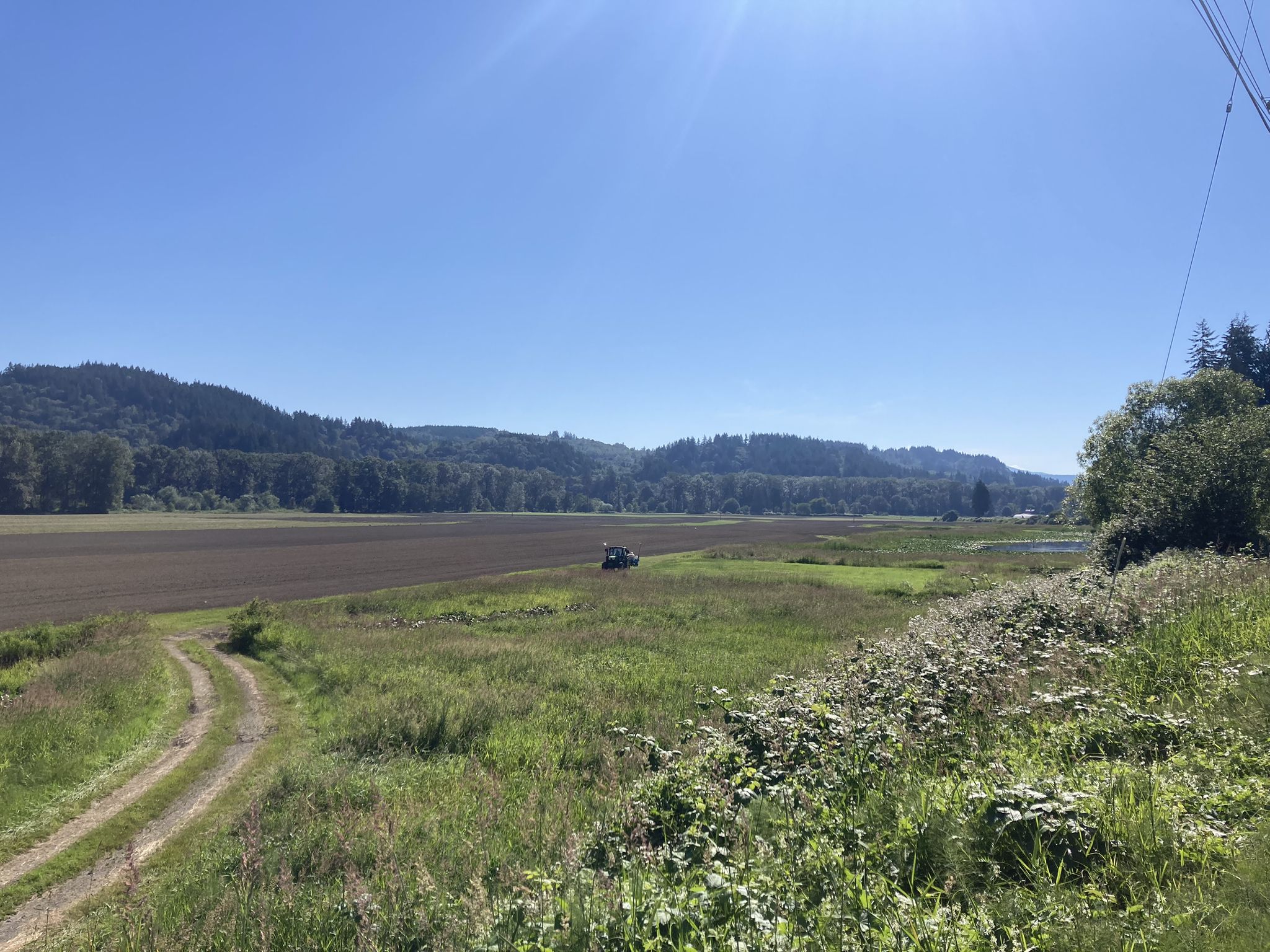 Sunny rural landscape with dirt road, fields, distant hills, and a tractor. - Sammamish River Trail – Views of the Sammamish River loop from Fales Road Parking Lot