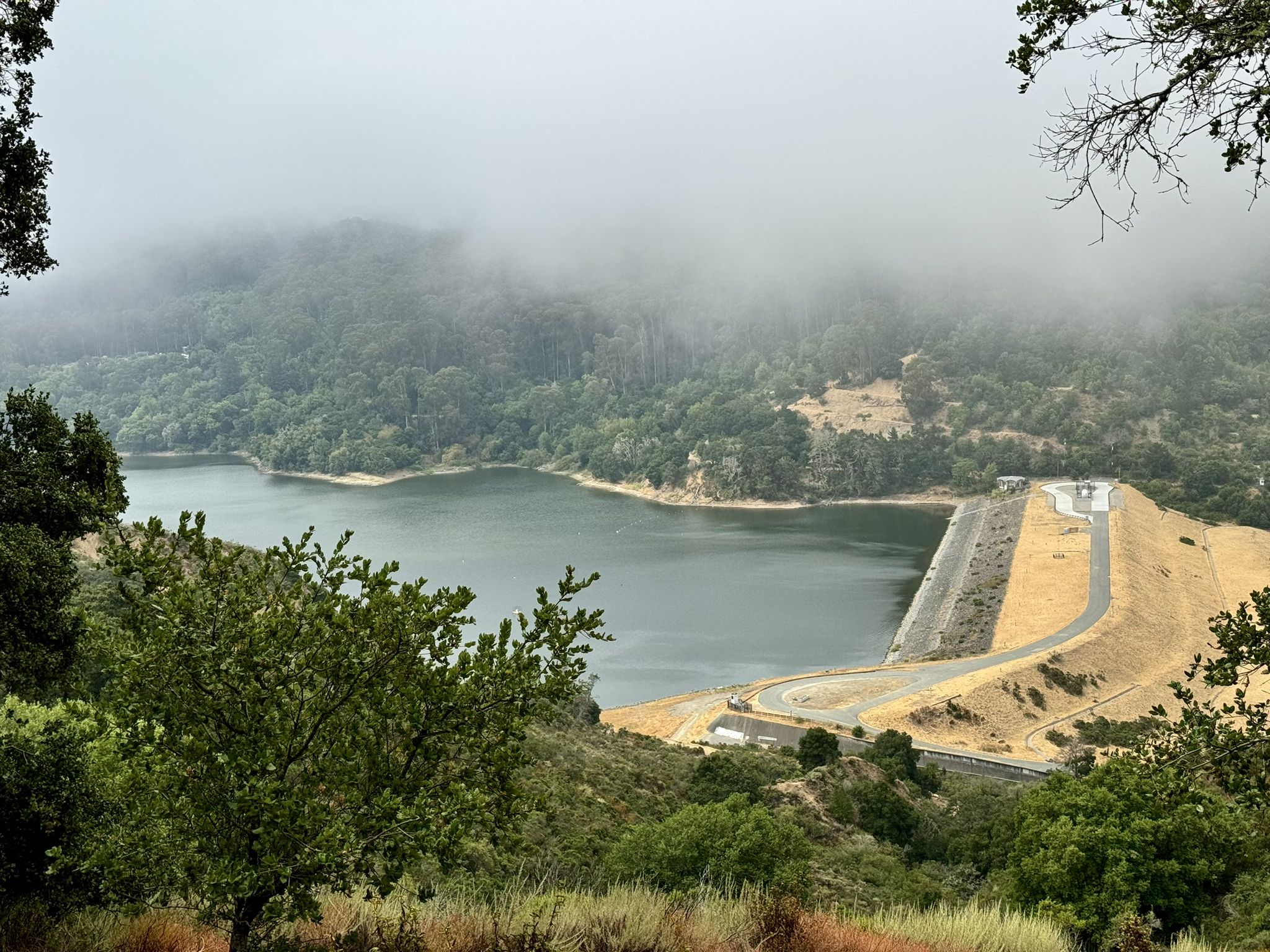 A large lake and dam nestled among foggy, forested hills under an overcast sky. - Sea Foam Loop Trail