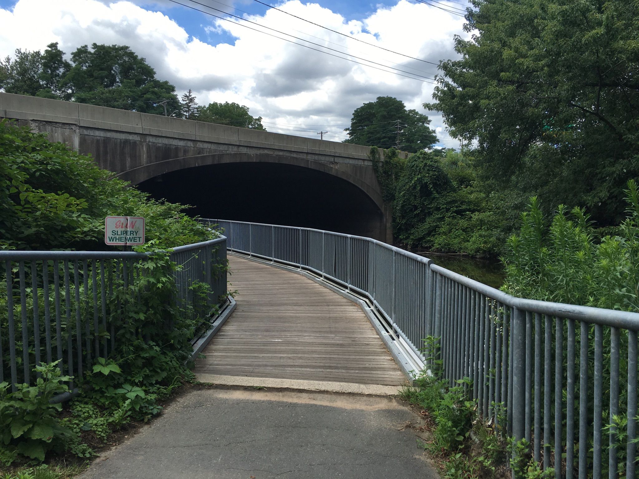 A wooden boardwalk with railings leading into a dark concrete underpass. - Saddle River County Park Bike Path