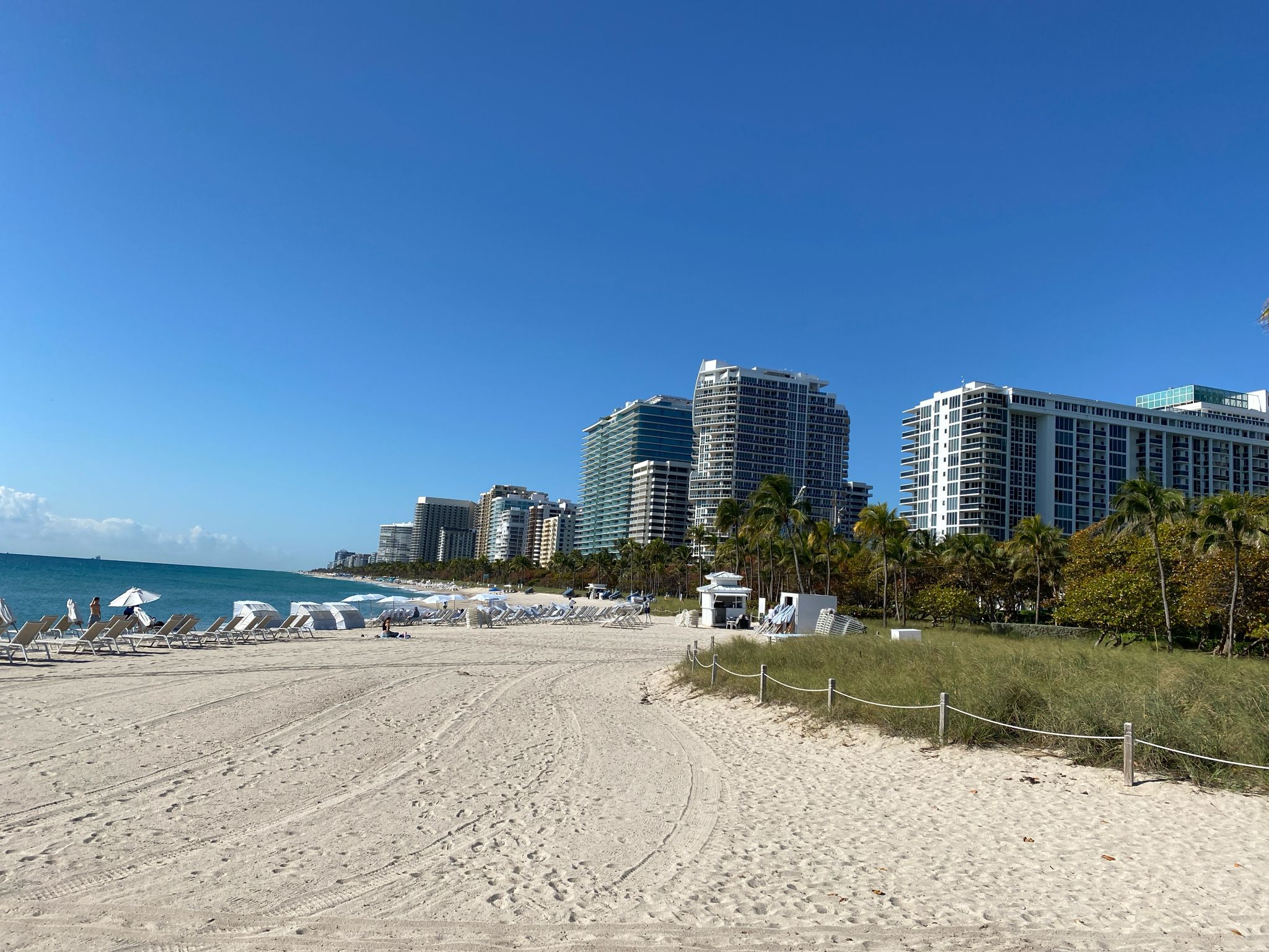 Sunny beach with ocean, distant city skyline, and beach chairs. - Bal Harbour Pier – Baker's Haulover Inlet loop from Surfside