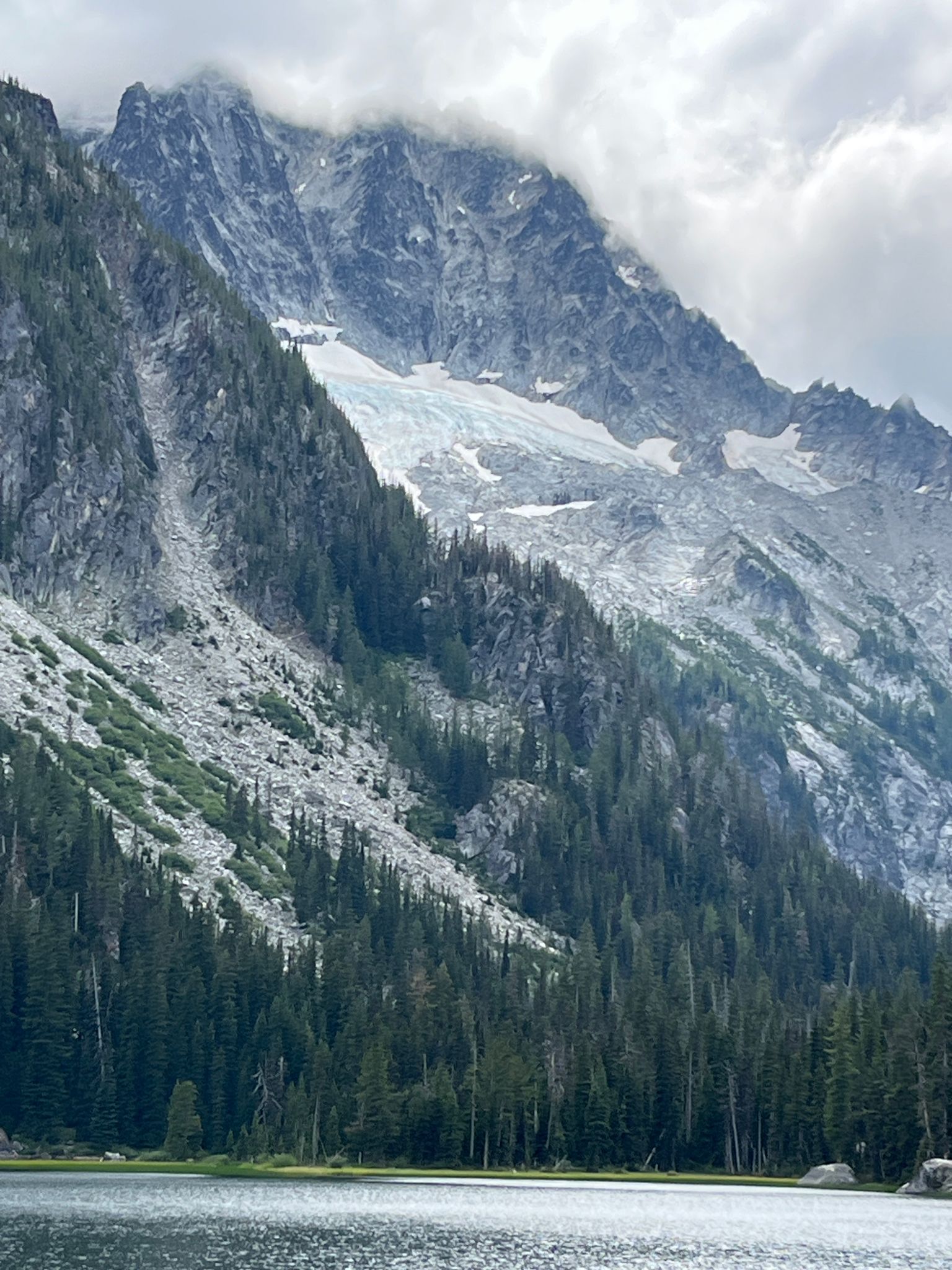 A steep mountain with a glacier and dense forest overlooking a lake. - Stuart Lake Trail