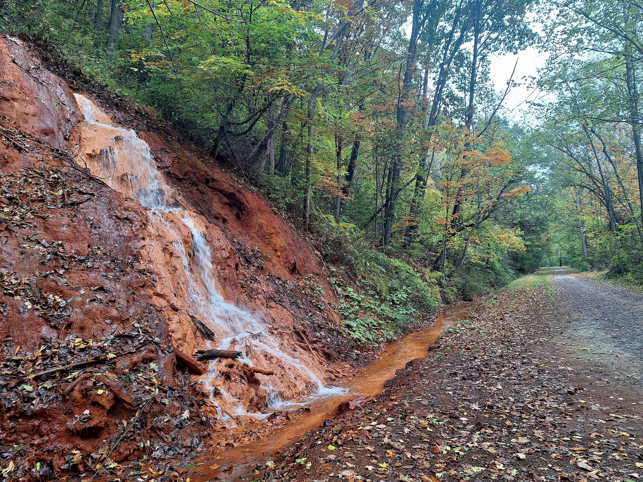 Orange-stained waterfall cascades down an embankment next to a path, autumn trees. - Red Waterfall loop from Versailles