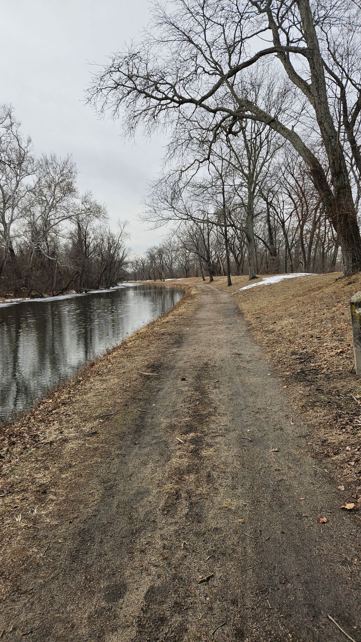 A dirt path runs alongside a calm canal with bare winter trees. - Lawrence Hopewell Trail – Brearley Oak tree loop from Mount Rose Preserve