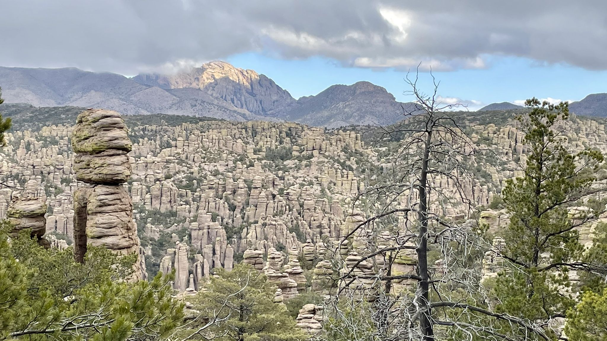 Rocky hoodoos and distant mountains under cloudy skies with green trees. - Heart of Rocks from Echo Canyon Trailhead