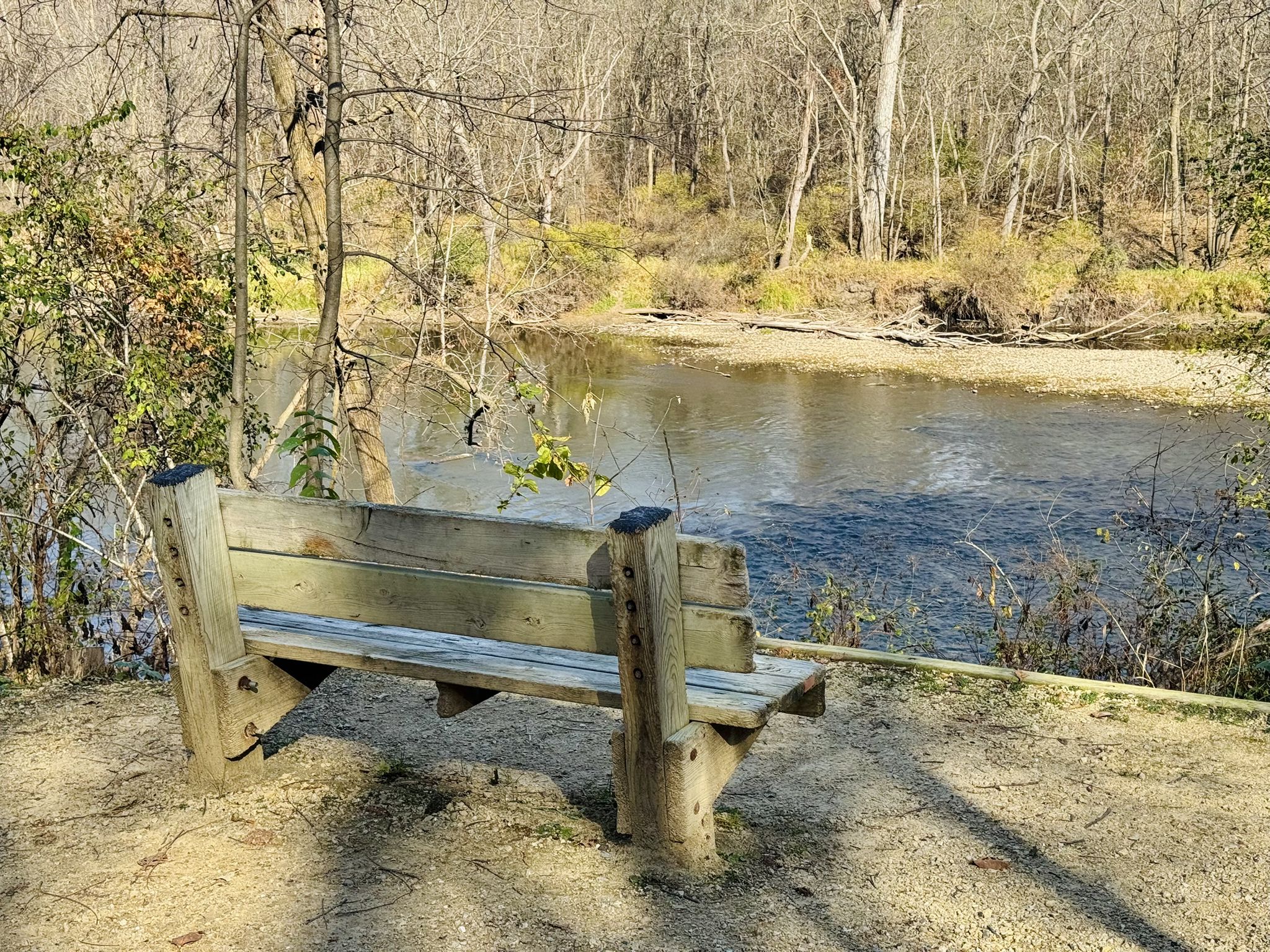 A rustic wooden bench on a dirt bank overlooking a calm river. - Lost without name