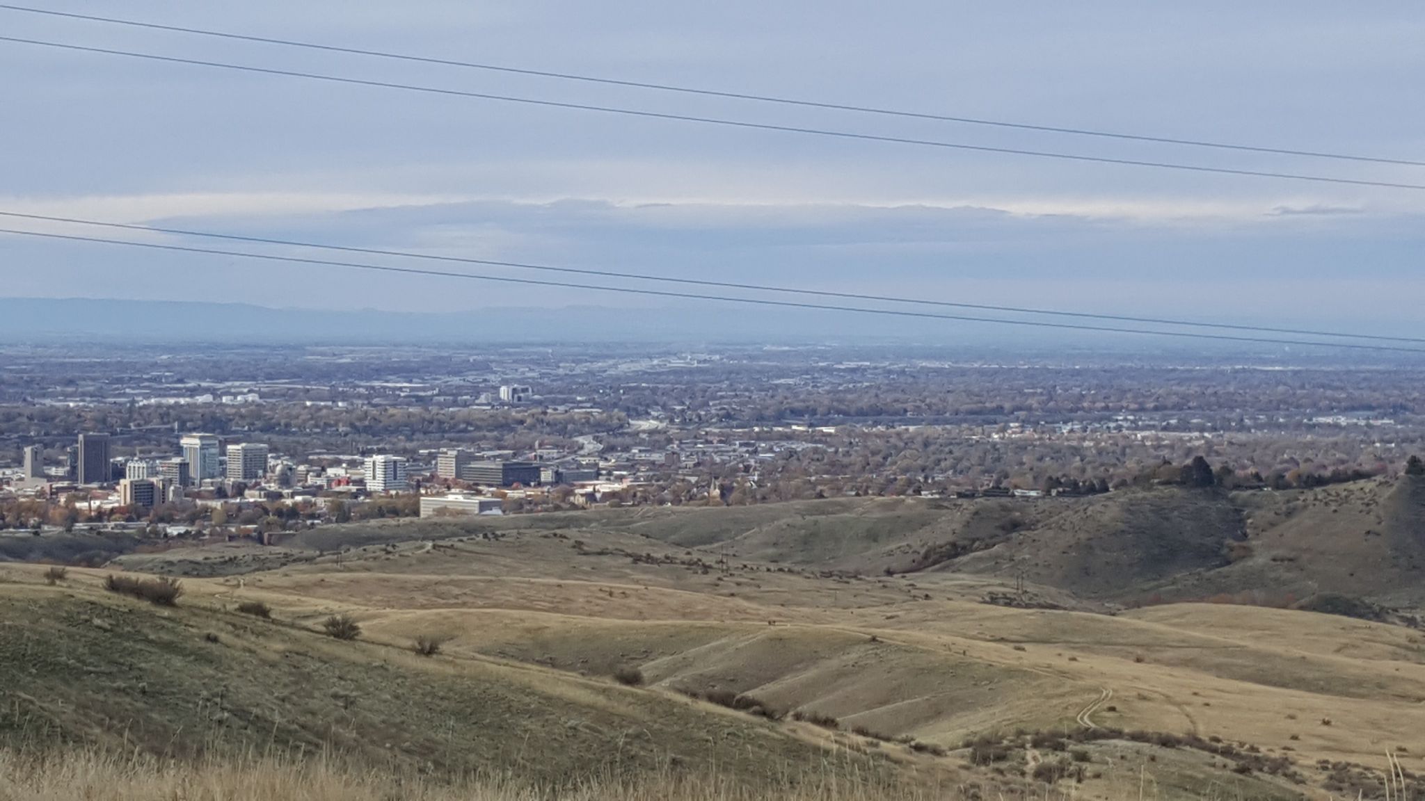 Overcast view of a distant city skyline beyond dry, rolling hills. - Military Reserve – Mountain Cove Trail loop from Boise