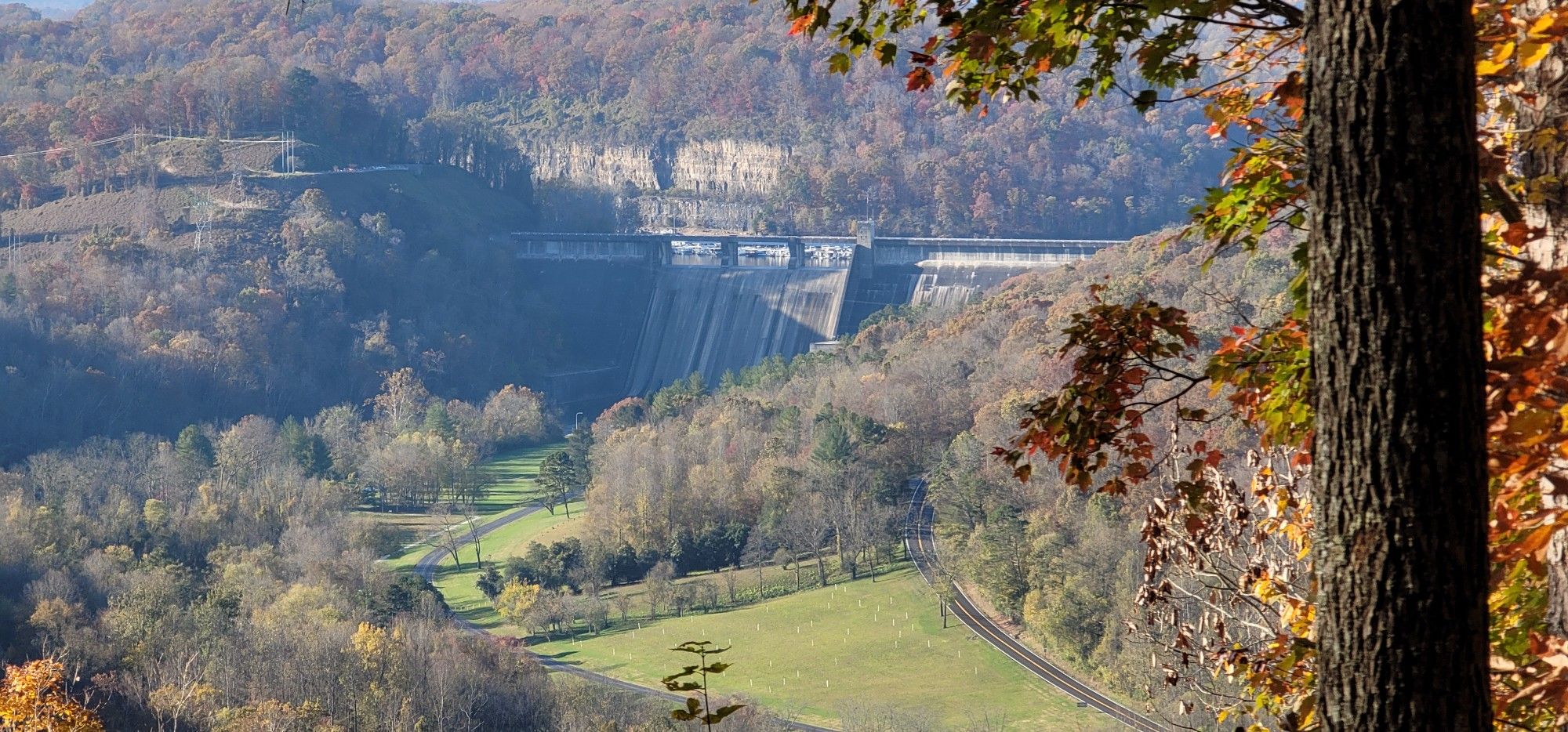 A large dam spans a forested valley under bright autumn sunlight. - Observation Point Trail