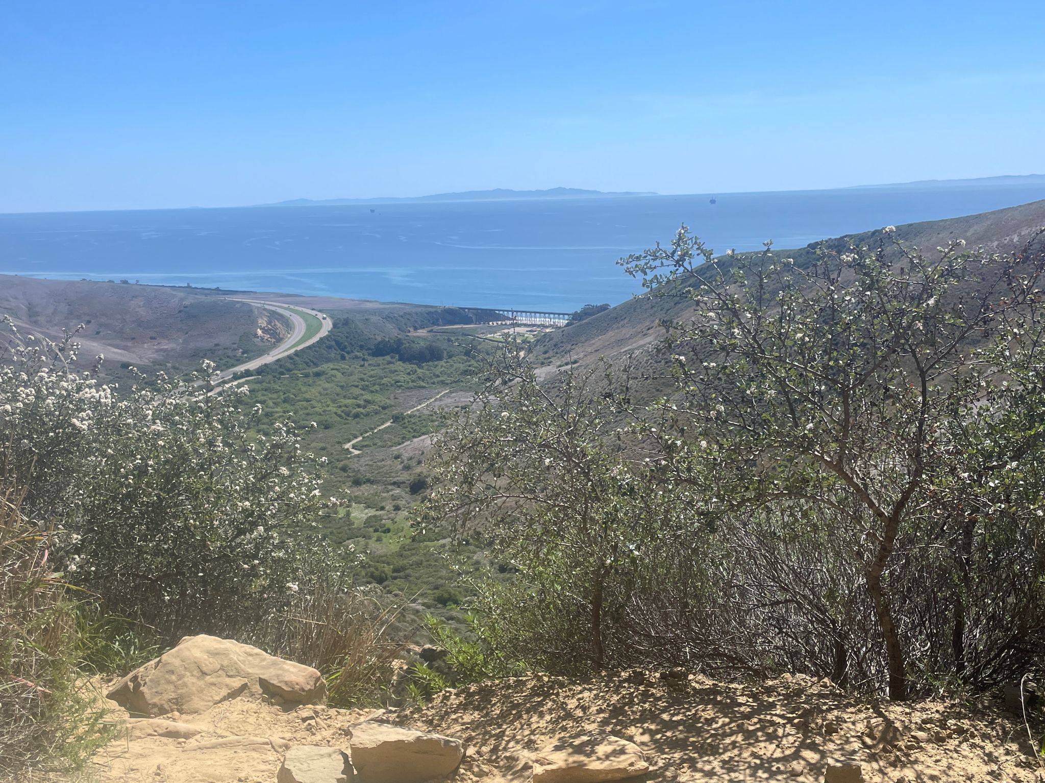 Sunny coastal view with a road winding through a valley to the ocean. - Gaviota Wind Caves Trail