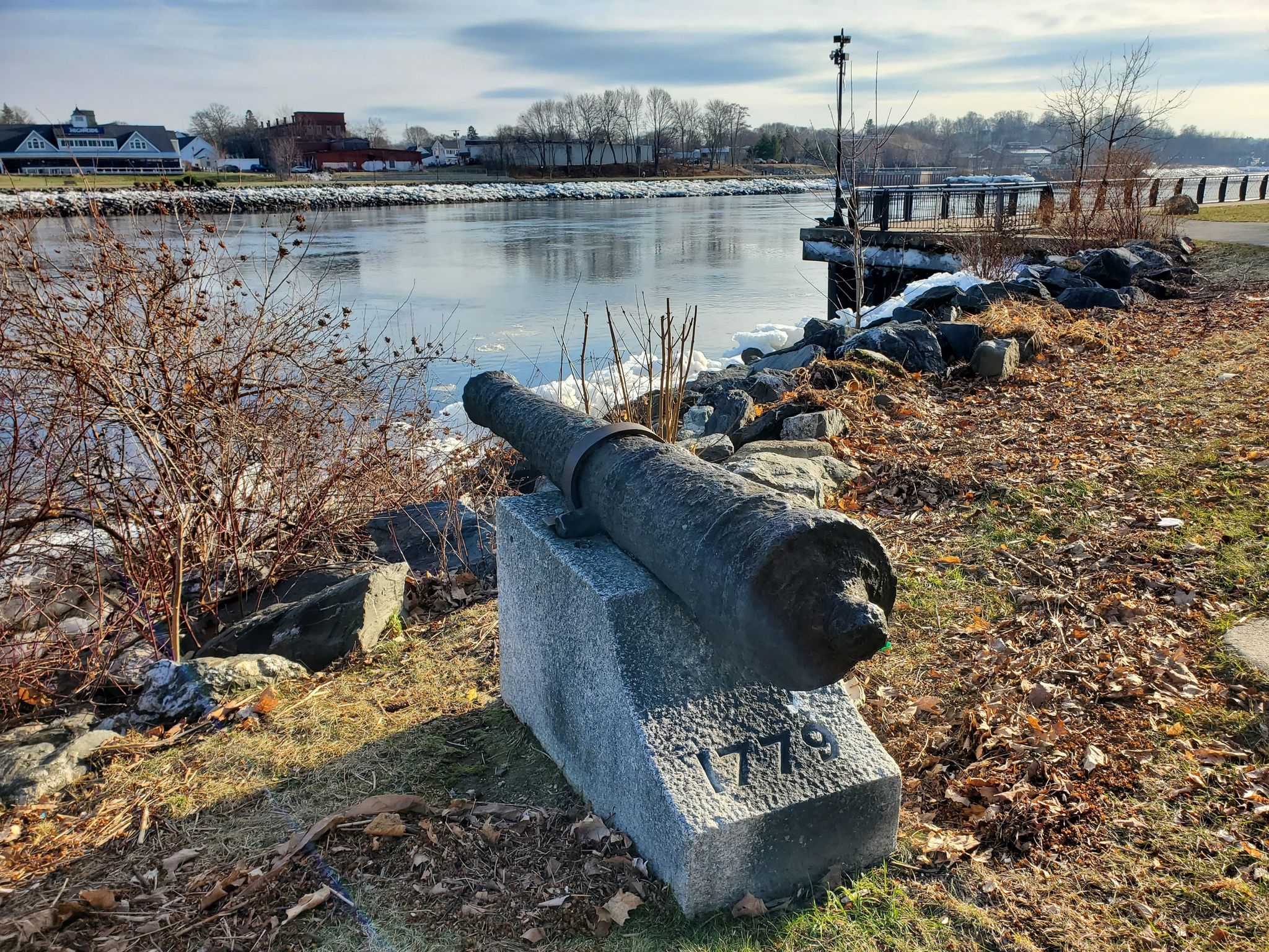Old cannon on a stone base by a partially frozen river, sunny. - East Coast Greenway: Bangor Waterfront Loop